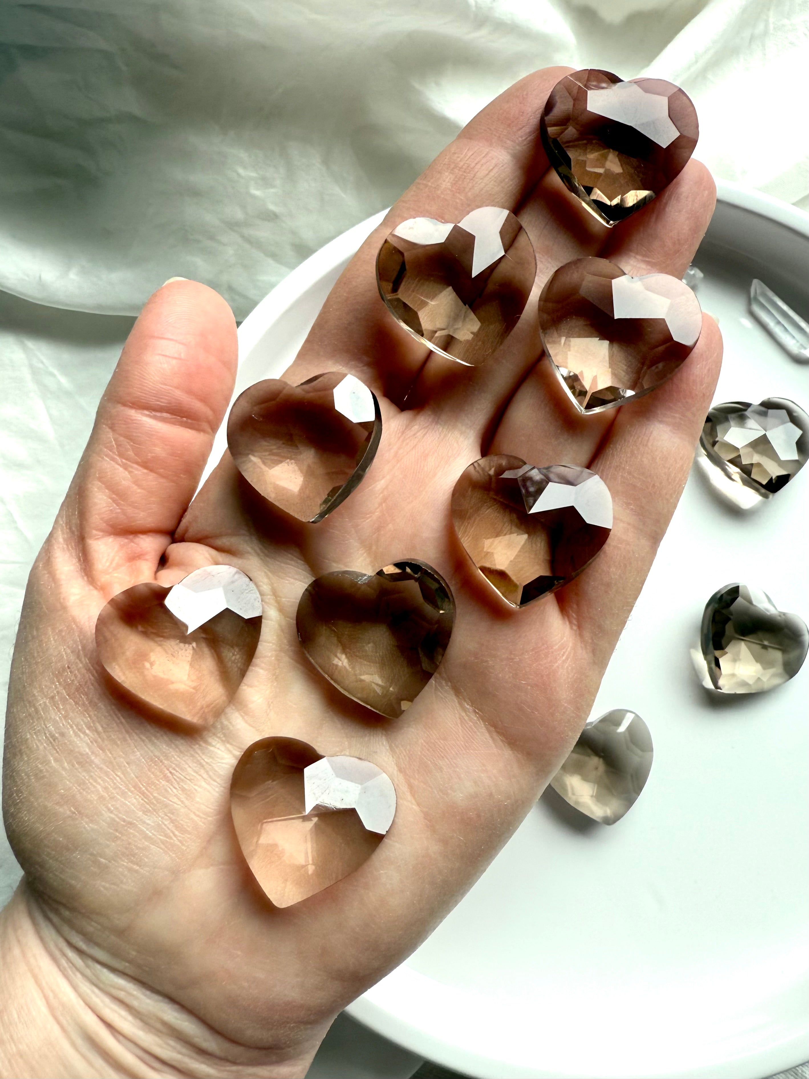 Smoky Quartz crystal hearts displayed on hand — faceted healing stones for grounding, meditation, energy protection, and Root Chakra alignment.