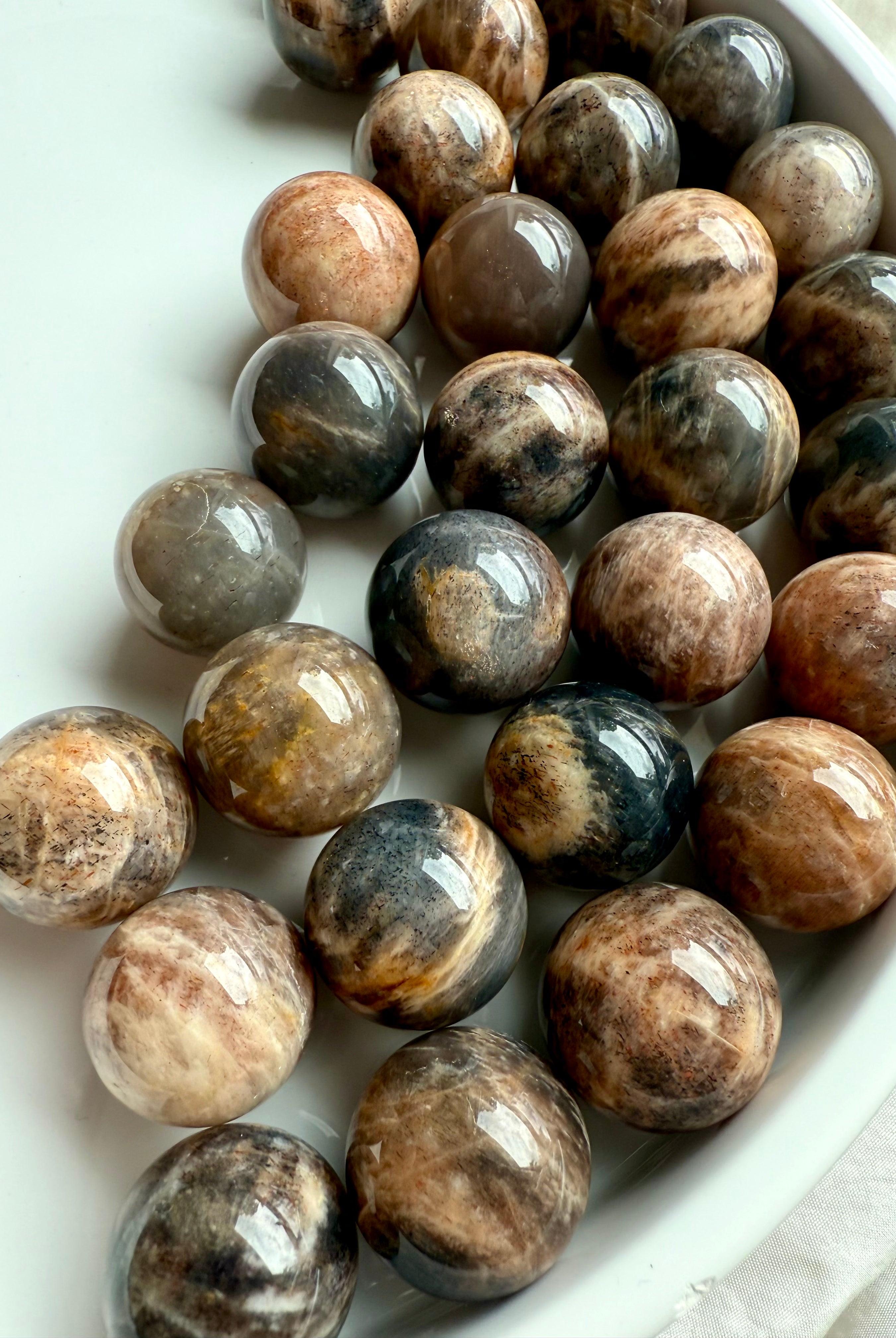 Mini Black Moonstone spheres on a white plate, showing dark shimmer & subtle flash — crystals for intuition, grounding, & feminine energy