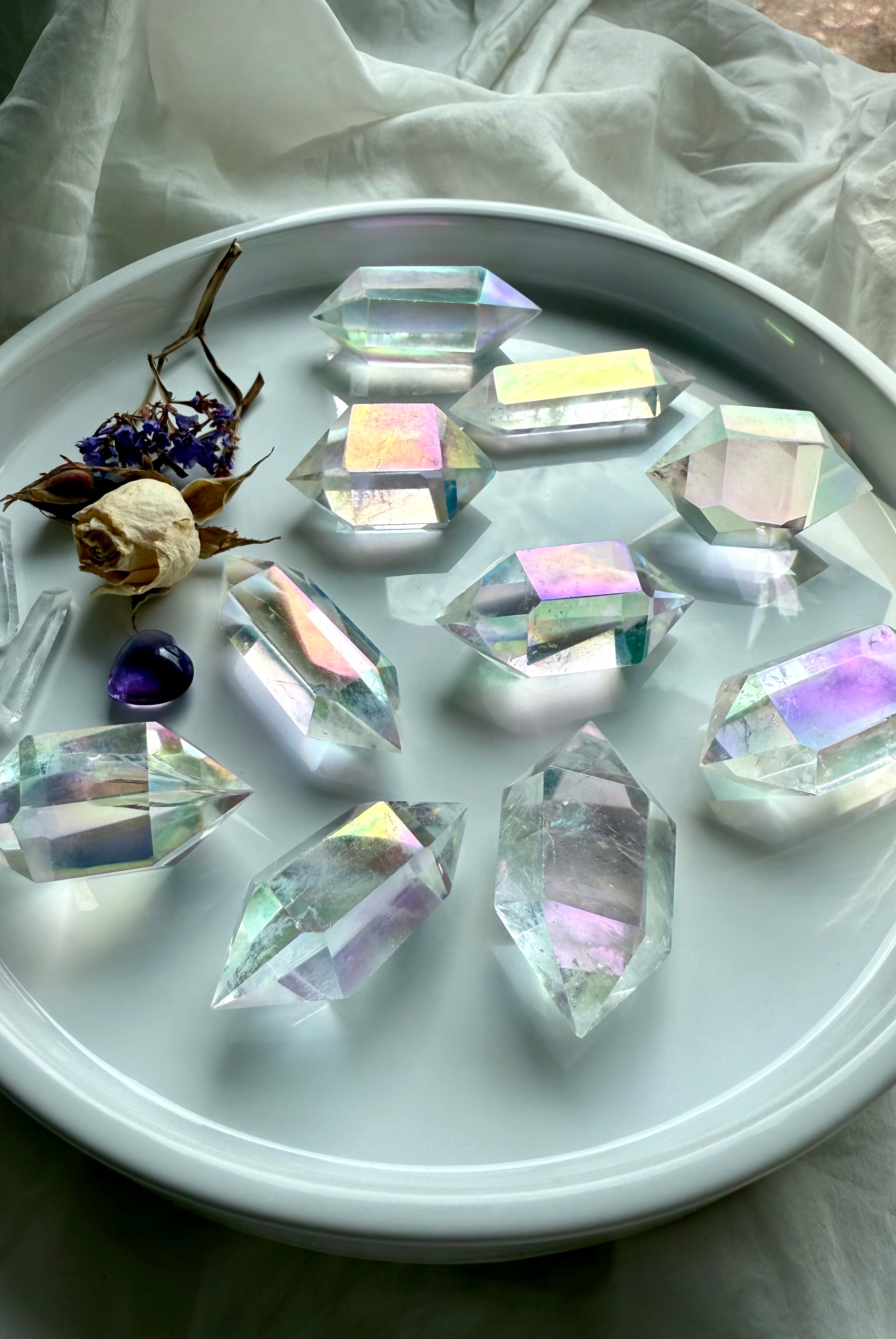 Collection of Angel Aura Quartz double terminated points arranged in a round dish with dried flowers and amethyst accent