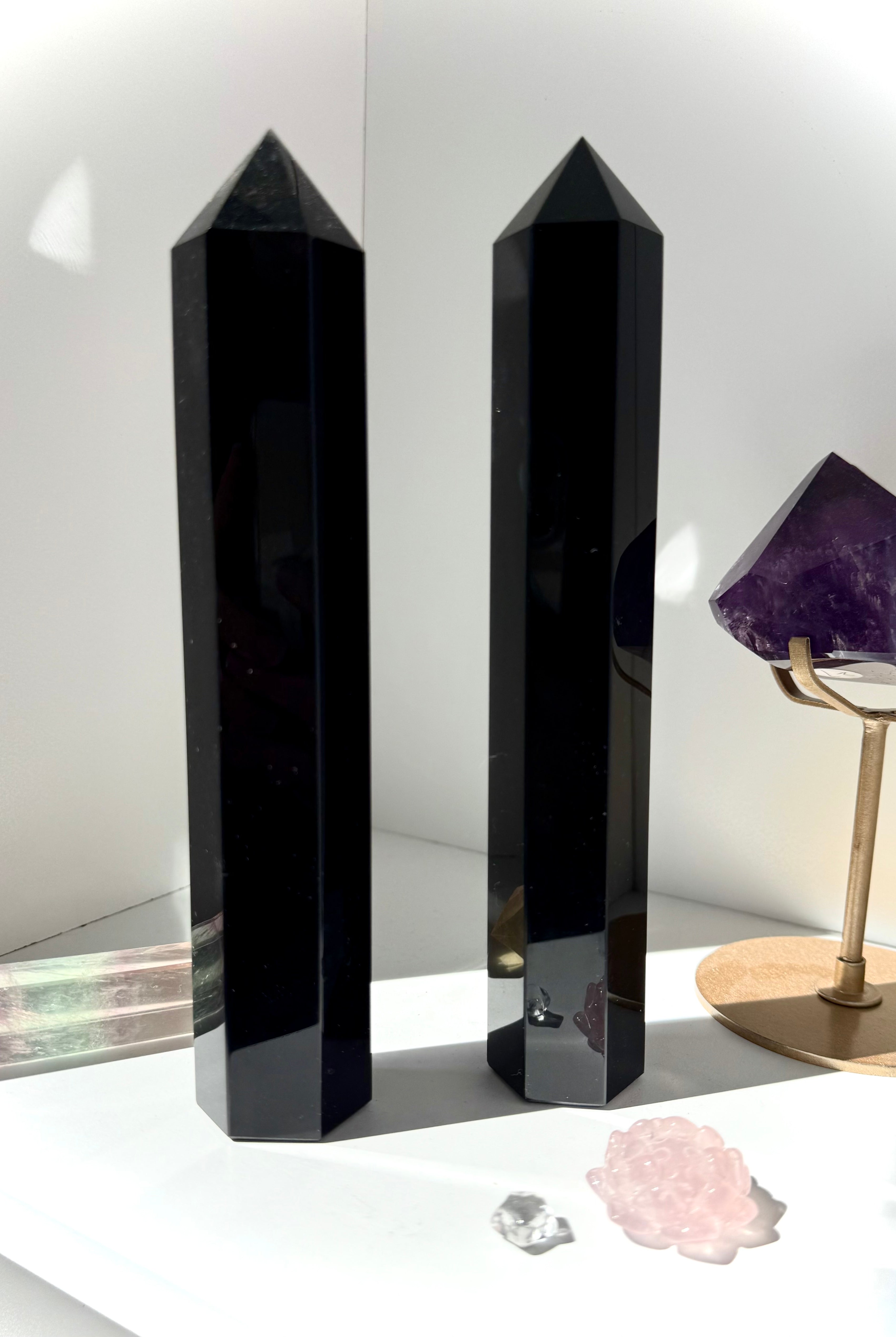 Two large Black Obsidian towers standing on a white shelf with other crystals — protective stones for home energy clearing.