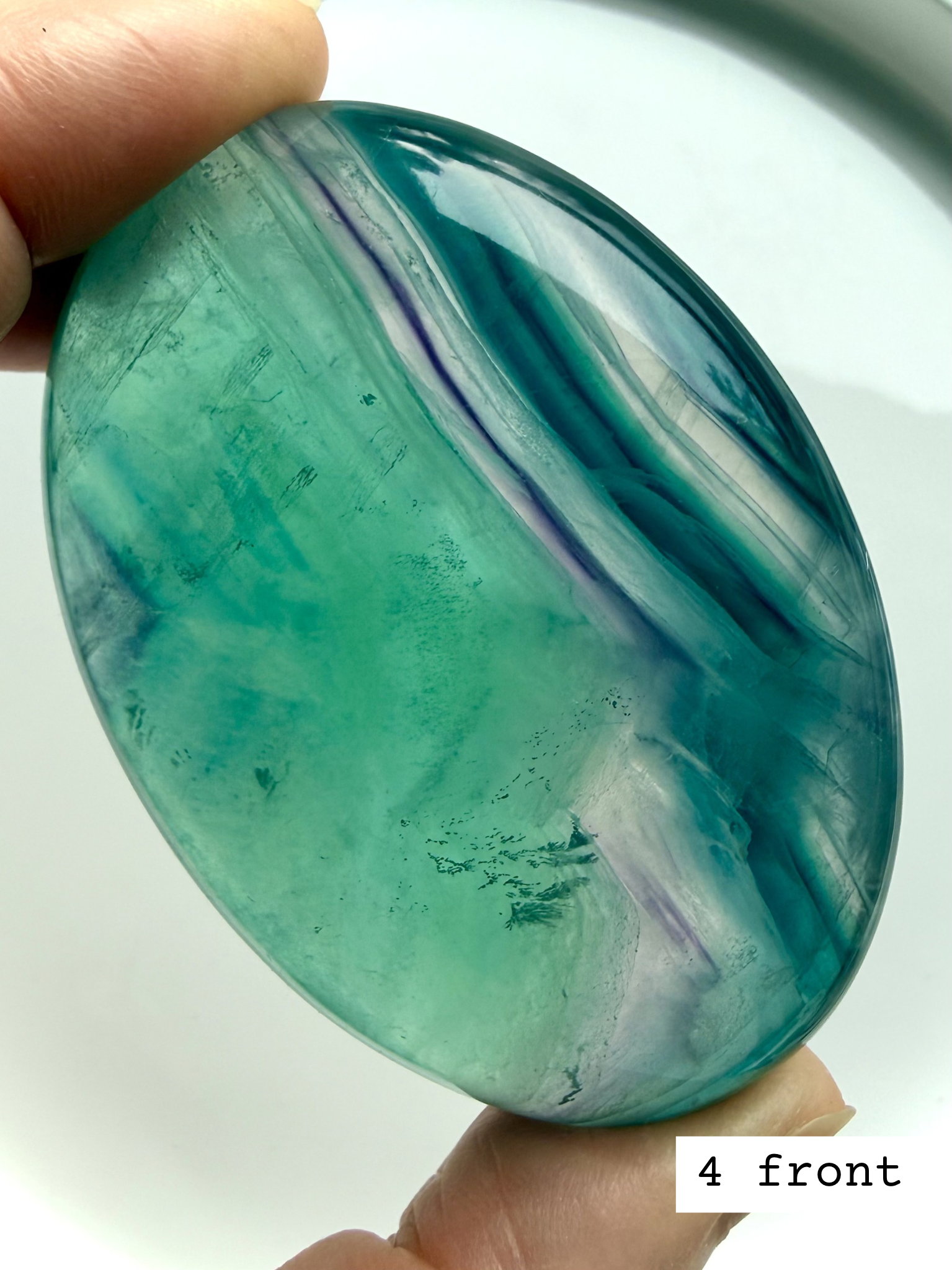 Teal fluorite palm stone #4 front view with vibrant blue green swirls and luminous glow in natural light