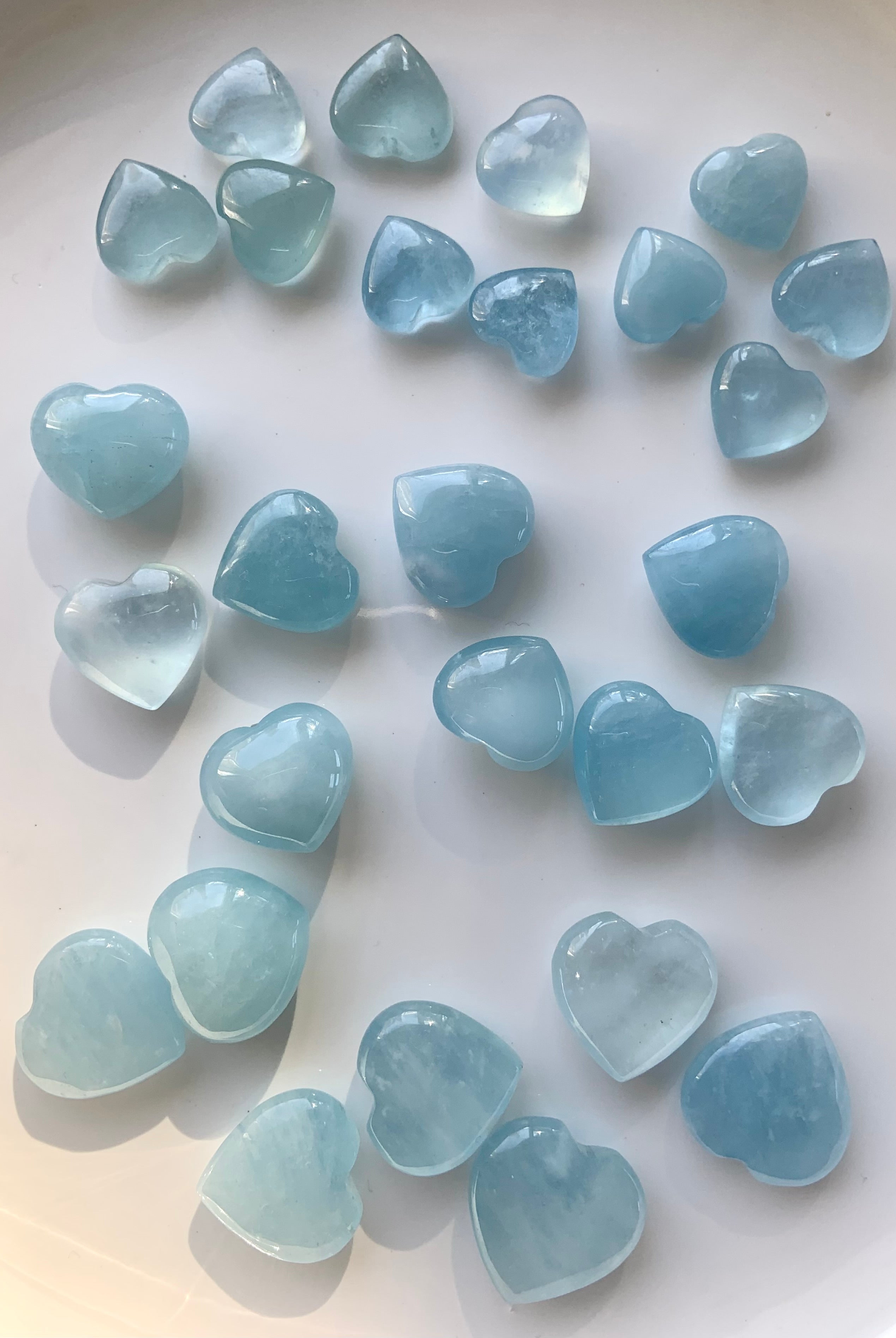 Array of Aquamarine hearts organized by size on a white surface — crystal heart carving collection in tranquil blue tones for throat chakra support.