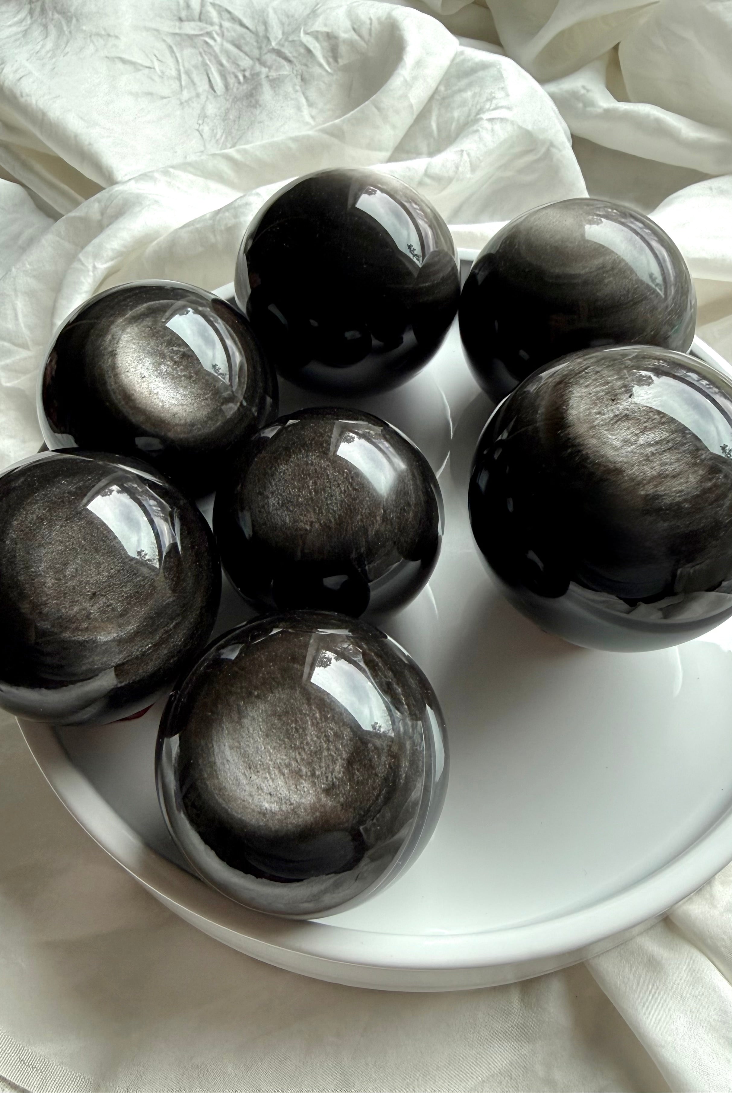 Collection of Silver Sheen Obsidian spheres arranged on tray, showing natural variations in silver flash and pattern