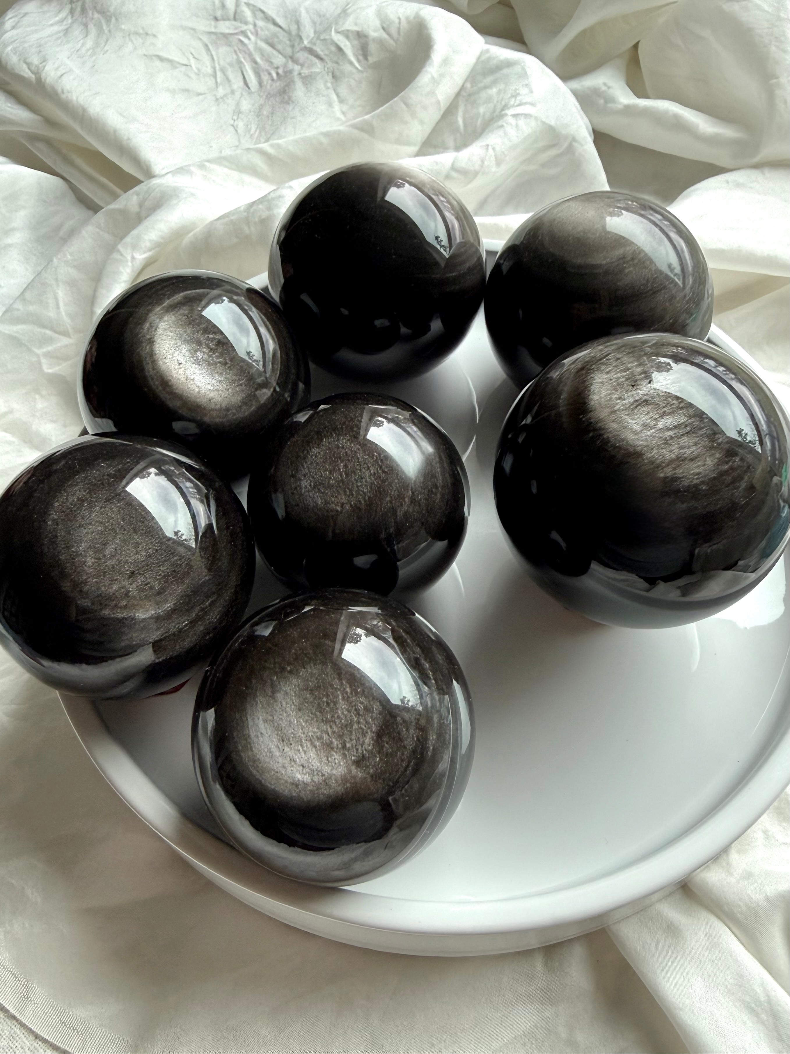 Collection of Silver Sheen Obsidian spheres arranged on tray, showing natural variations in silver flash and pattern