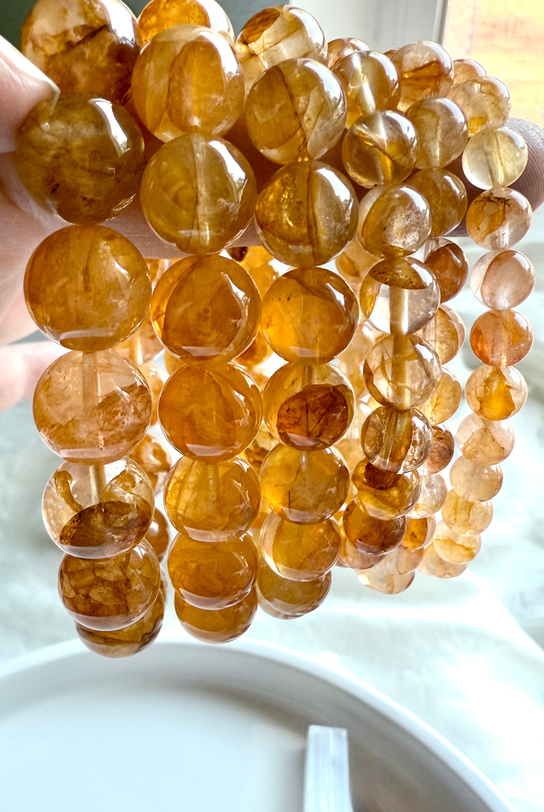 A row of six Golden Healer Quartz bracelets from large to small beads, held to the light to show luminous golden tones and natural clarity.