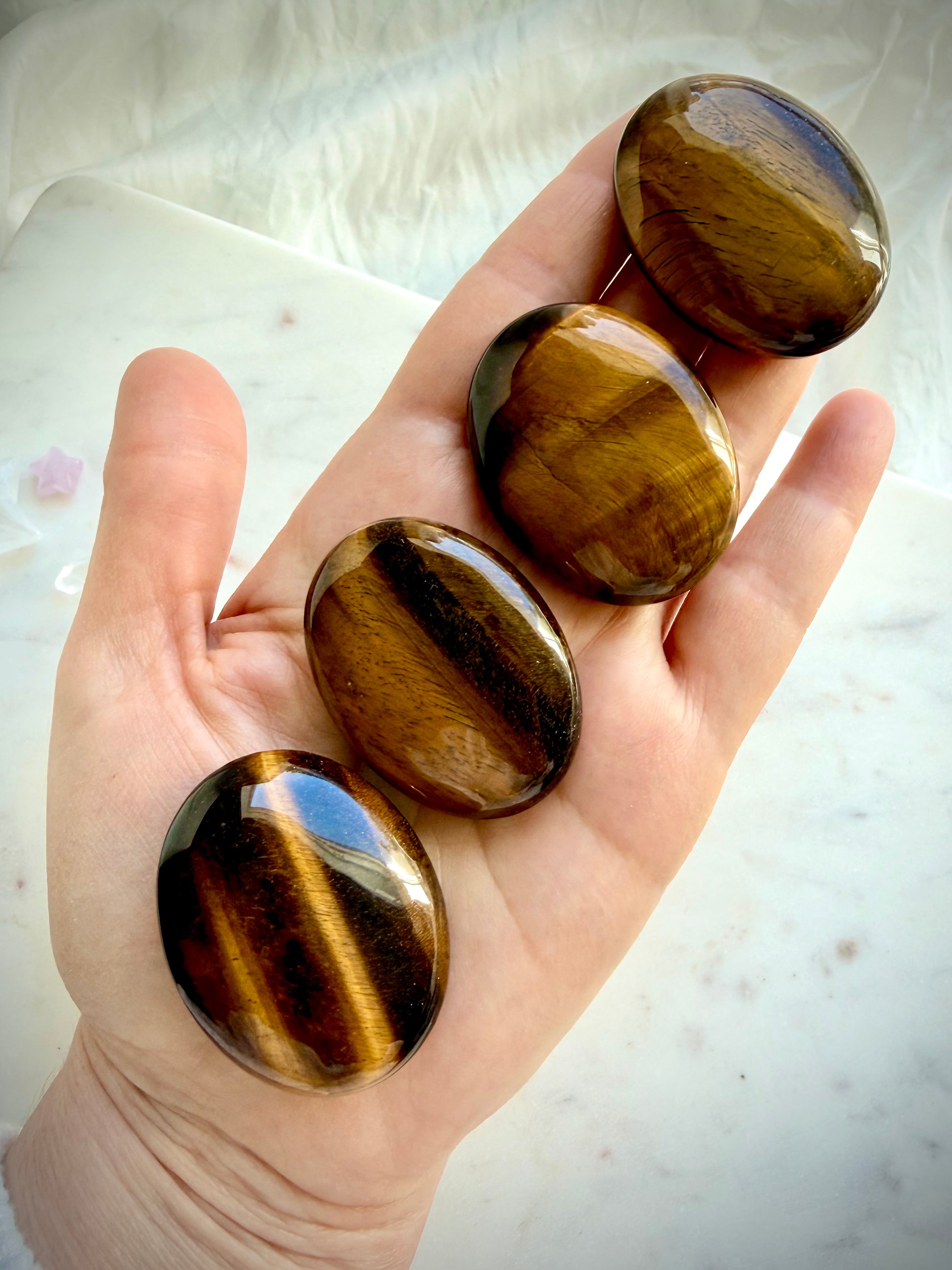 Hand holding polished Tiger’s Eye palm stones with rich golden flash and natural chatoyant bands