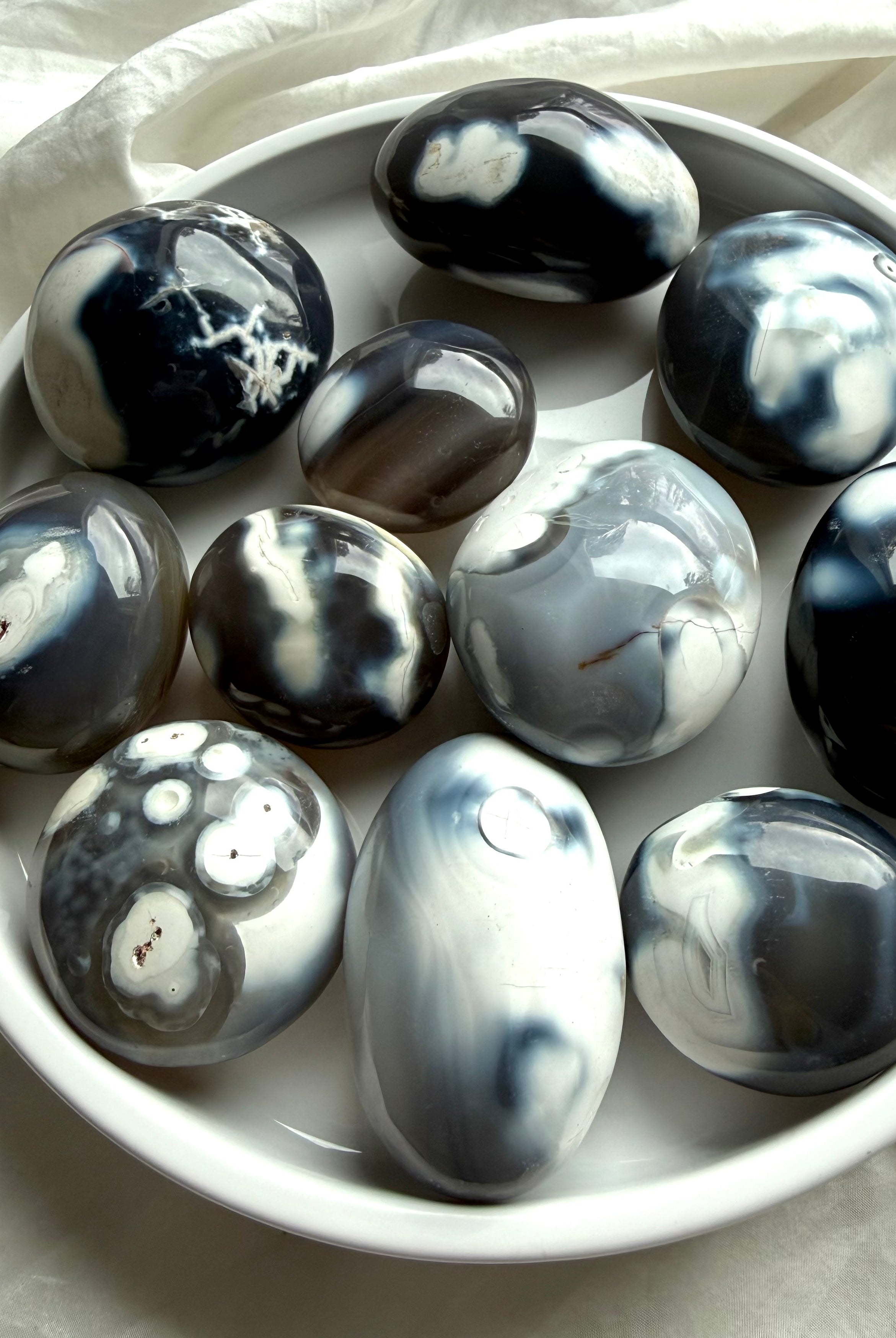 Orca Agate palm stones displayed in a ceramic bowl, featuring soft black, white, and gray patterns for calm and emotional grounding