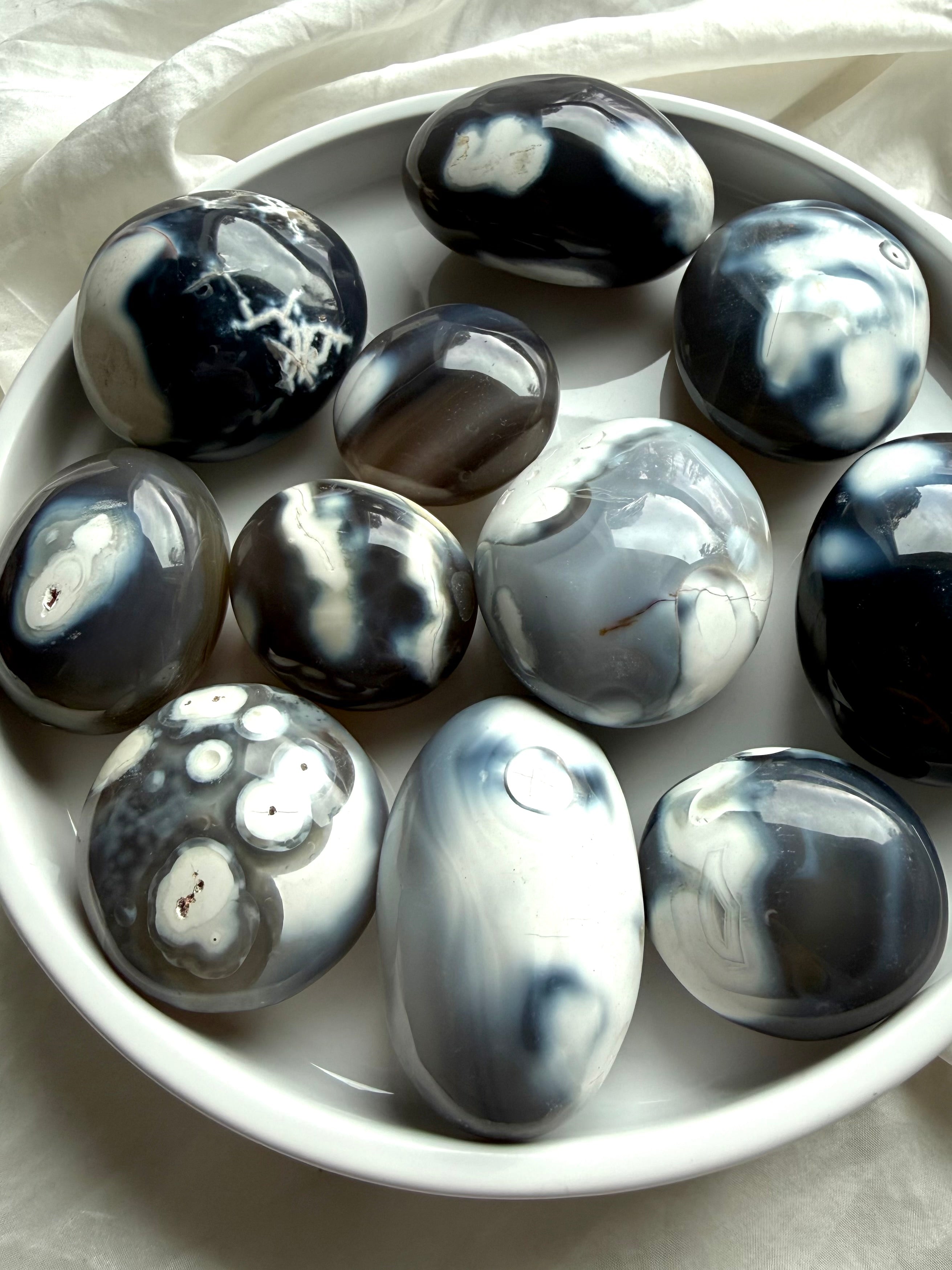 Orca Agate palm stones displayed in a ceramic bowl, featuring soft black, white, and gray patterns for calm and emotional grounding