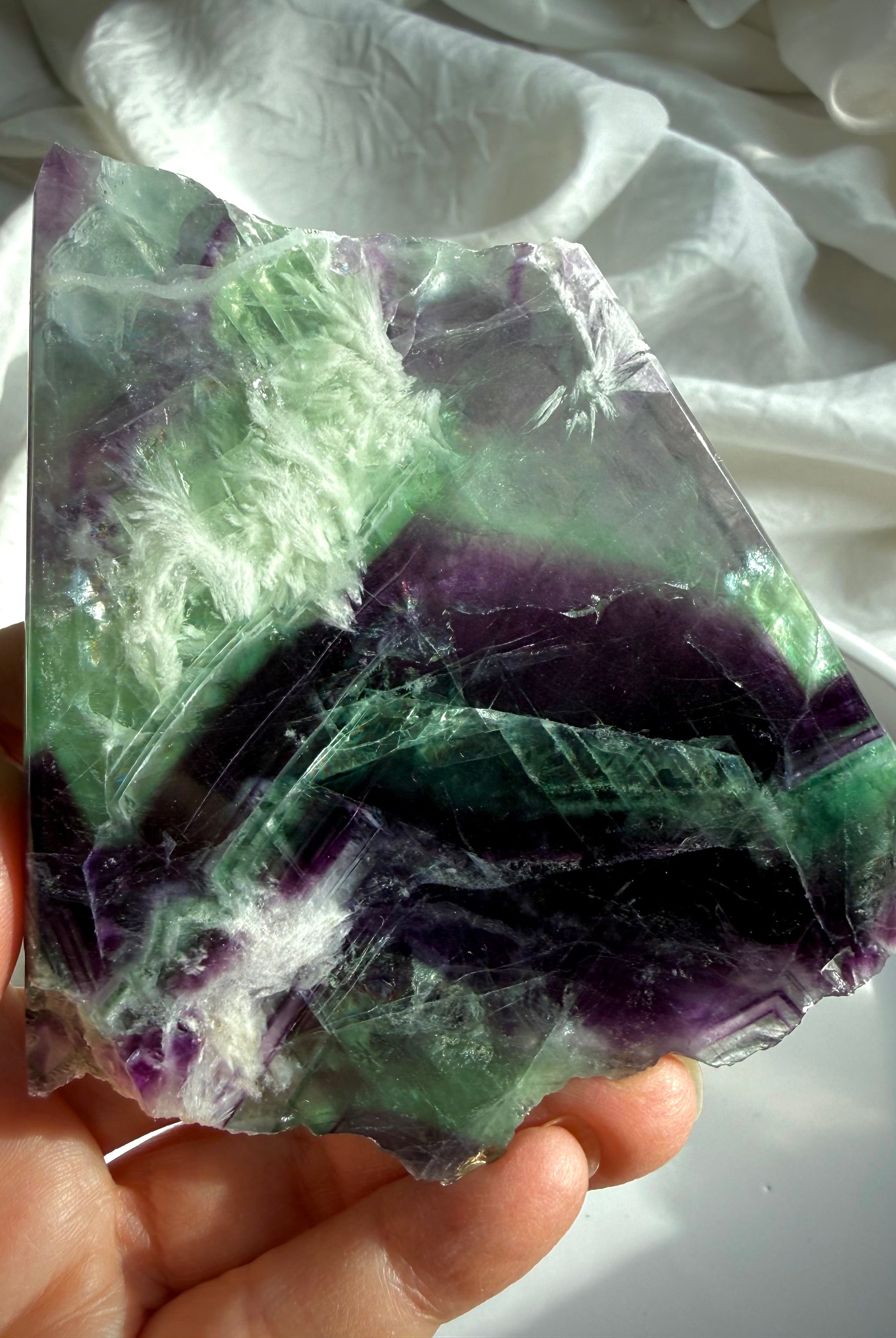 Polished fluorite slab photographed in natural light highlighting layered green and violet color zoning with rainbows