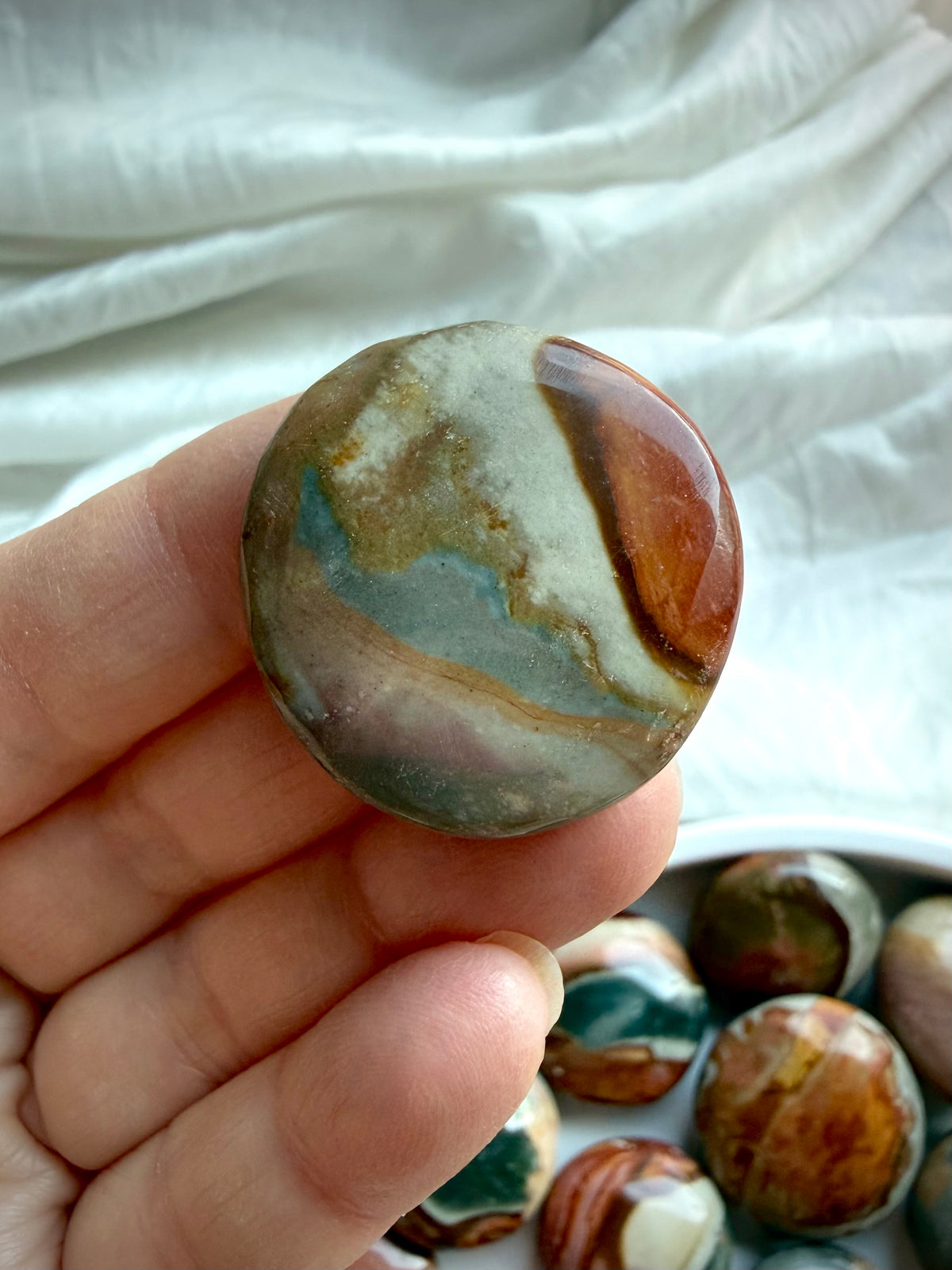 Mini Polychrome Jasper palm stone with soft sage green, rust, and golden tan landscape patterns, held between fingers