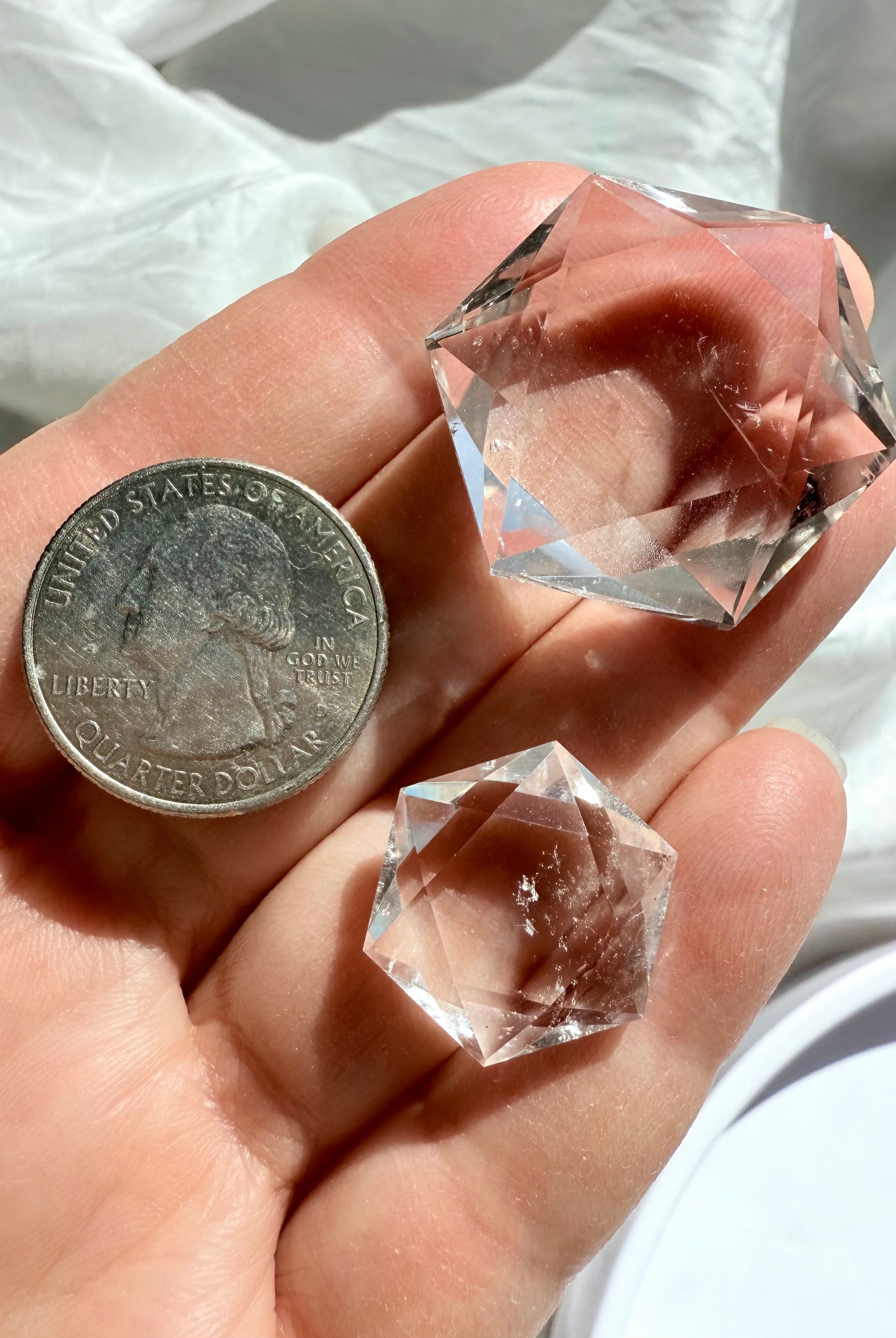 Both sizes of faceted Clear Quartz hexagons shown on hand with quarter for scale reference