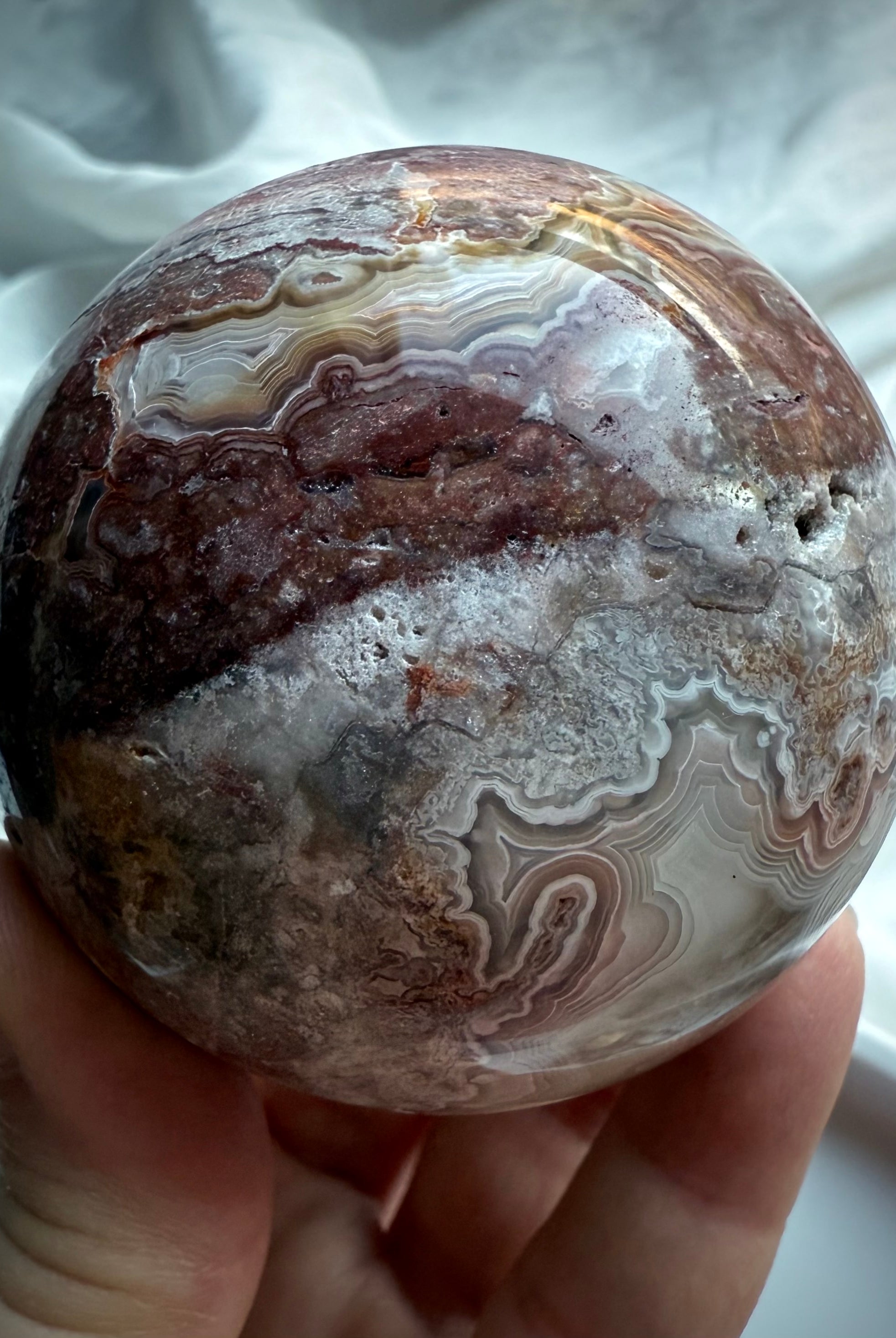 Polished gemstone sphere with swirling cream and plum-colored agate patterns and druzy crystal pocket