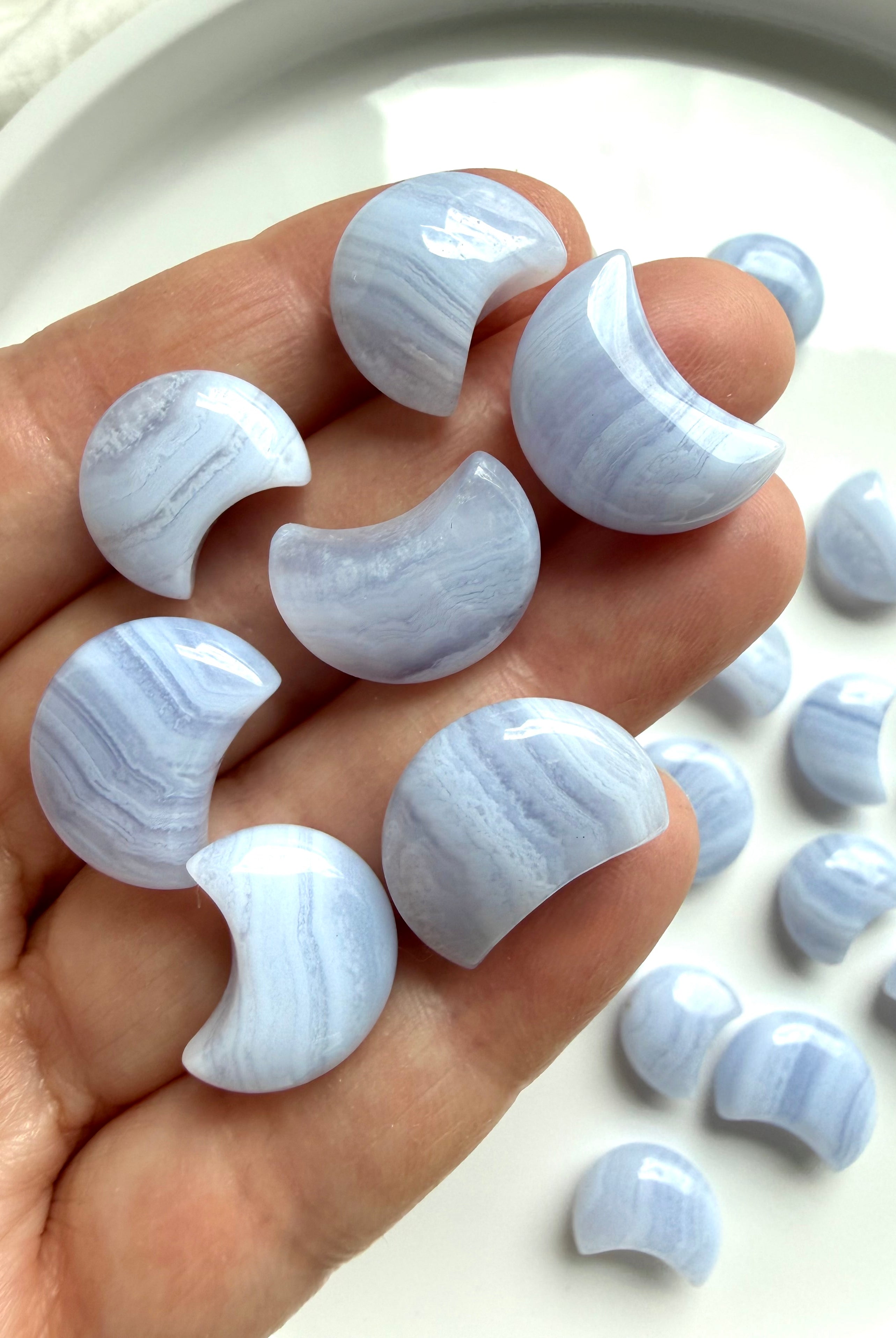 Hand holding polished Blue Lace Agate crescent moon carvings showing the three available size options