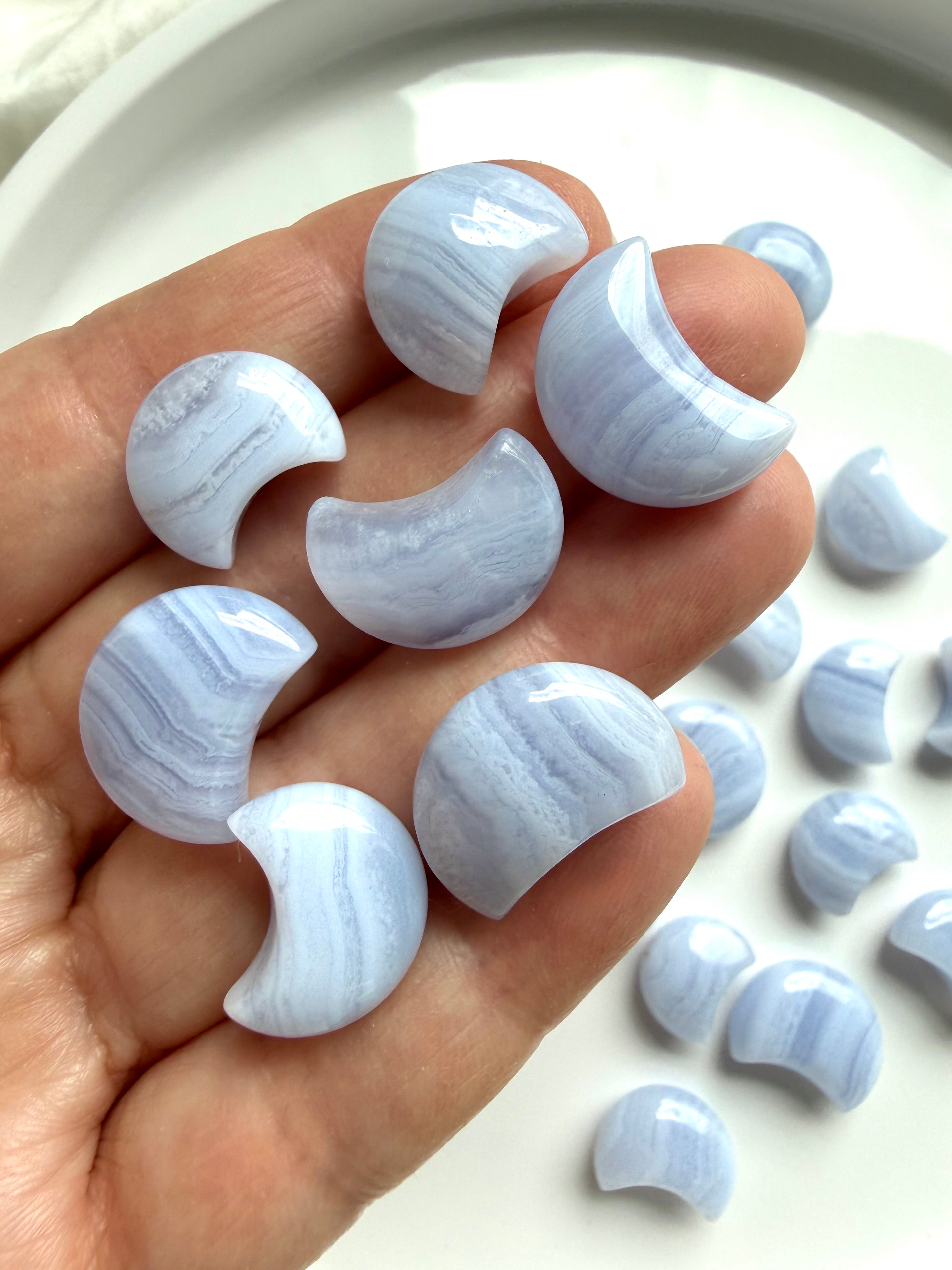 Hand holding polished Blue Lace Agate crescent moon carvings showing the three available size options