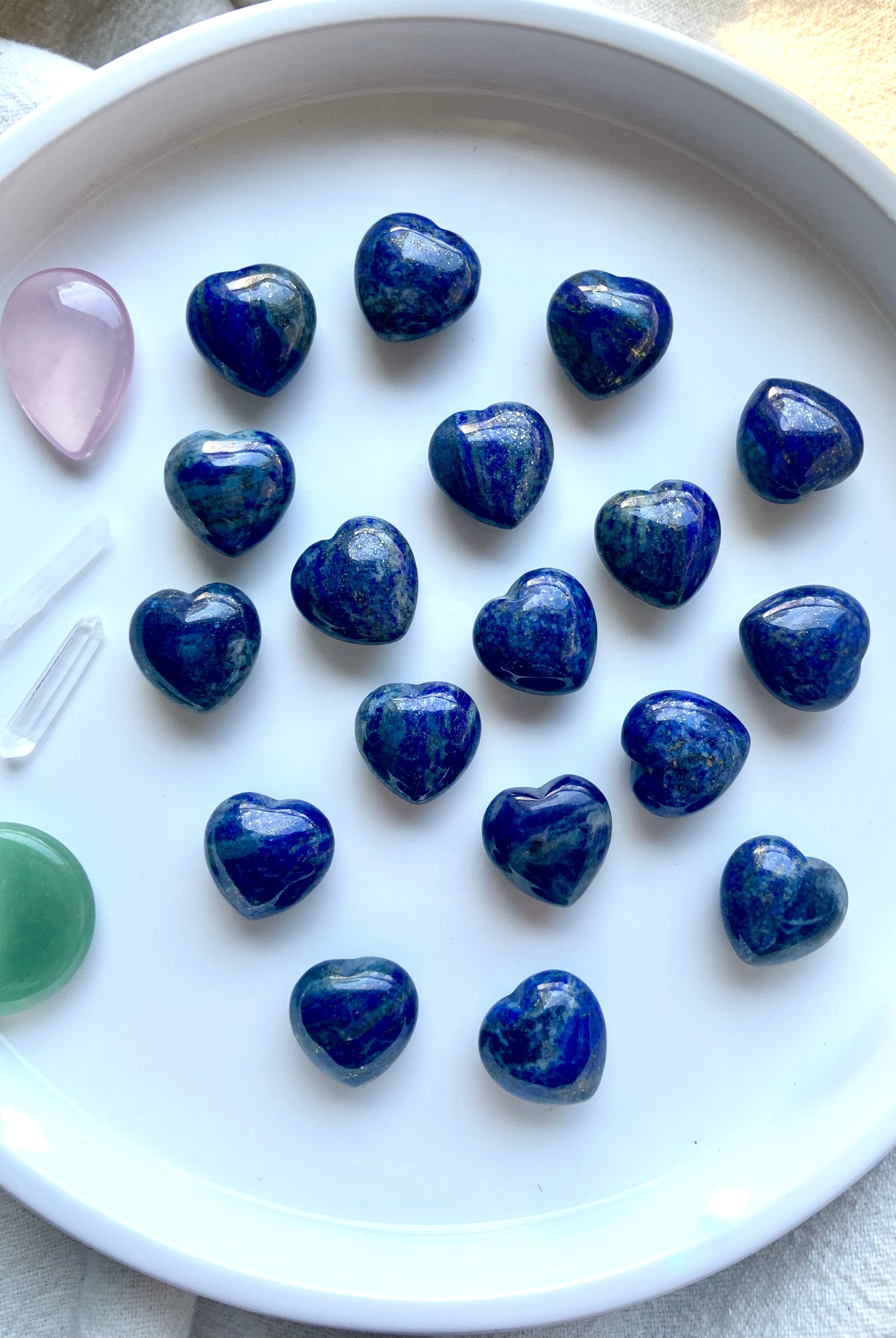 our mini sized, blue Lapis Lazuli Hearts shown on a white plate with some other crystal shapes as accents