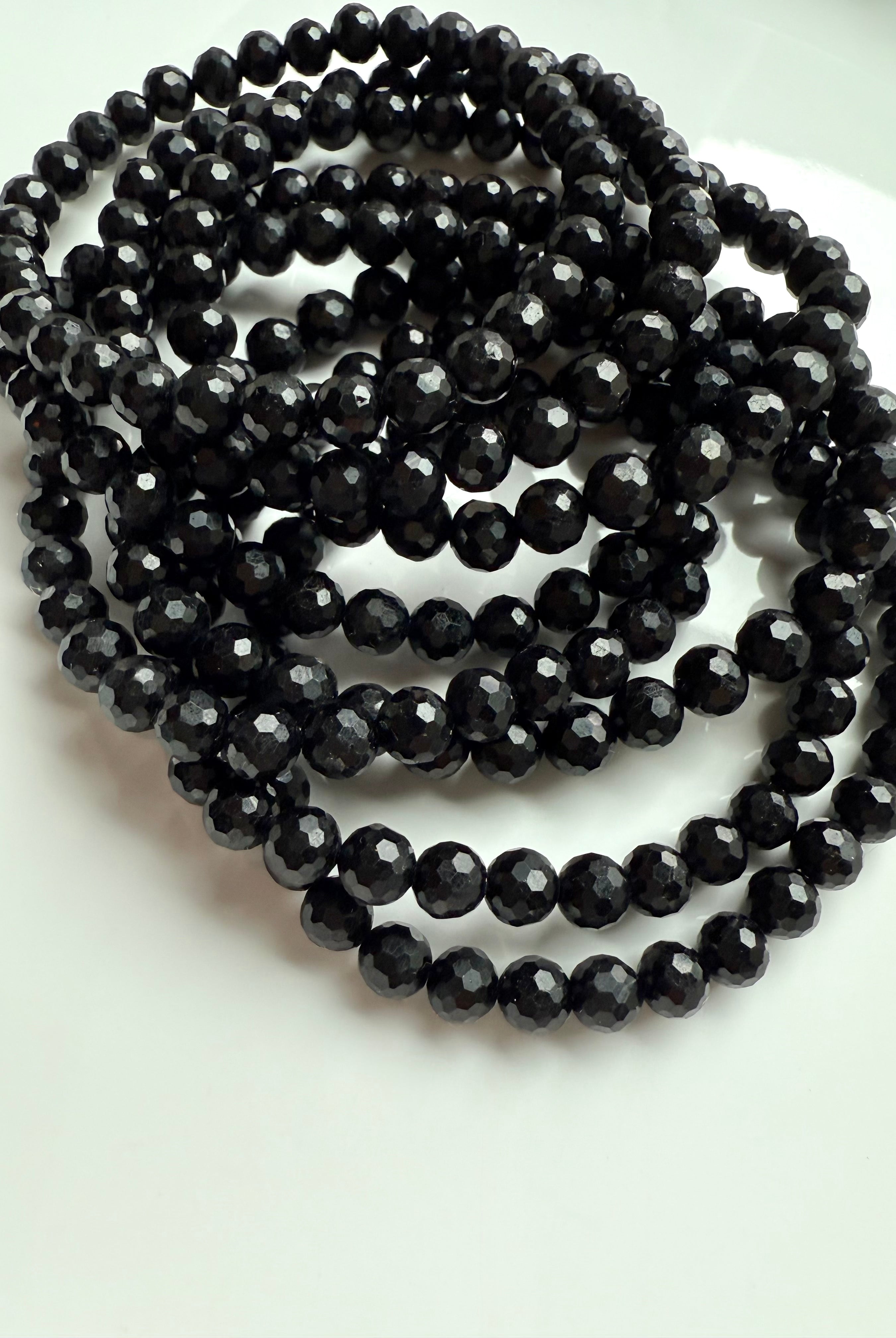 pile of faceted black tourmaline stretch bracelets coiled on white dish, ready for crystal protection ritual