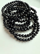 pile of faceted black tourmaline stretch bracelets coiled on white dish, ready for crystal protection ritual