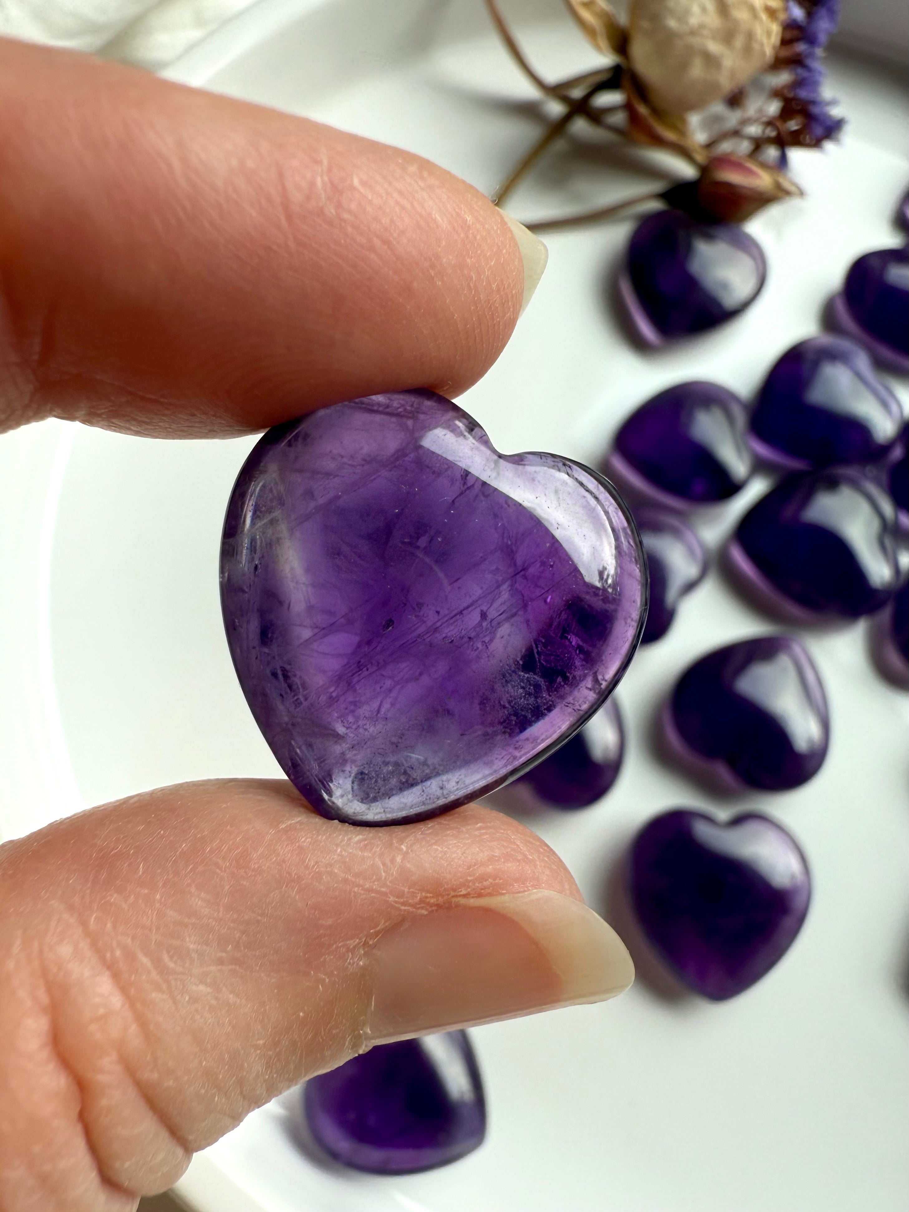 Amethyst crystal heart held between fingers showing translucent purple color and subtle inclusions — crown chakra stone for intuition and spiritual connection.
