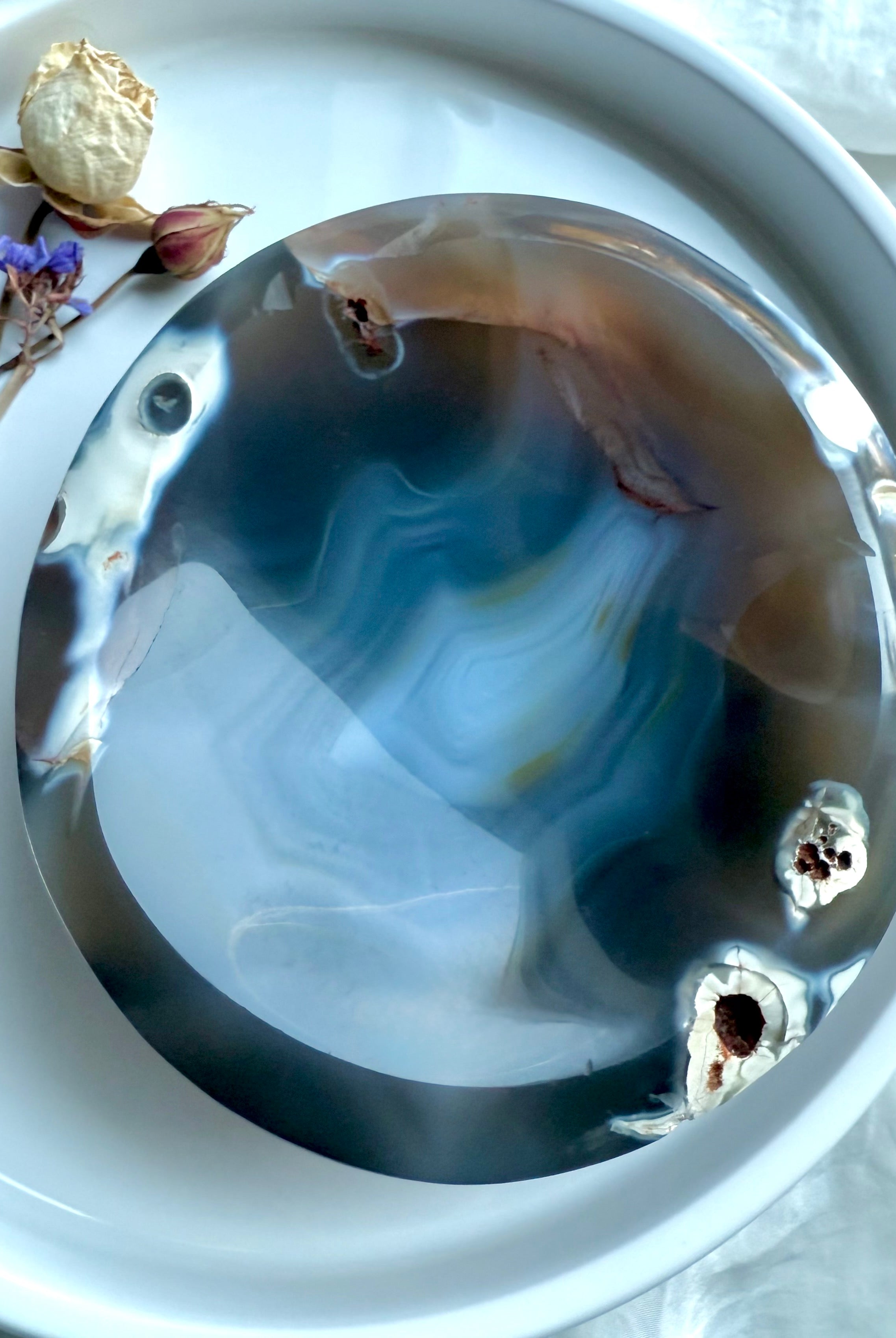 Overhead photo of polished Orca Agate crystal bowl on a white tray with dried flowers, selenite, and palo santo for cleansing rituals