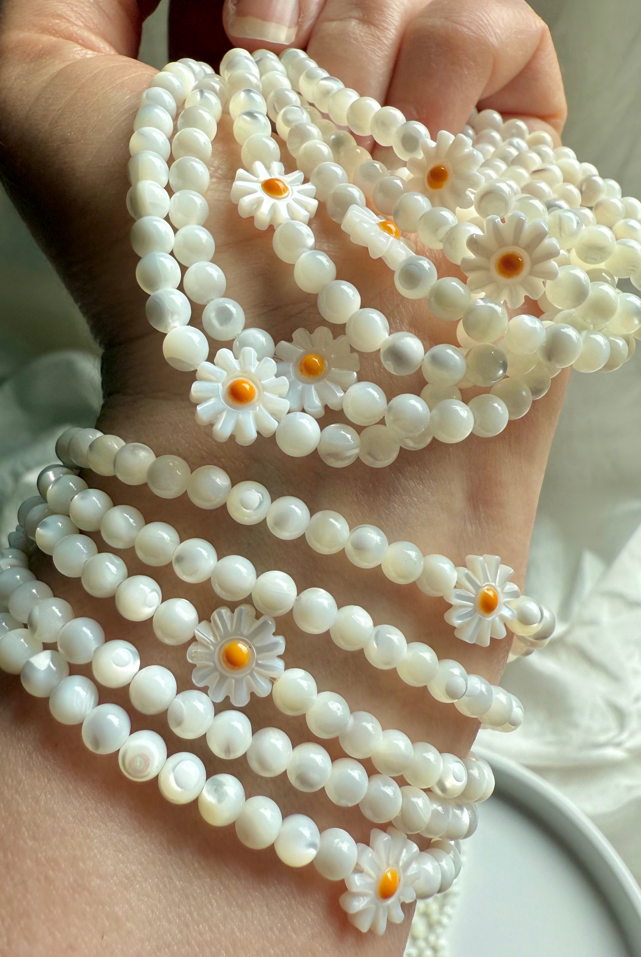 Close-up of Mother of Pearl daisy flower beads on opalescent white shell bracelet – floral gemstone jewelry for joy and lightness