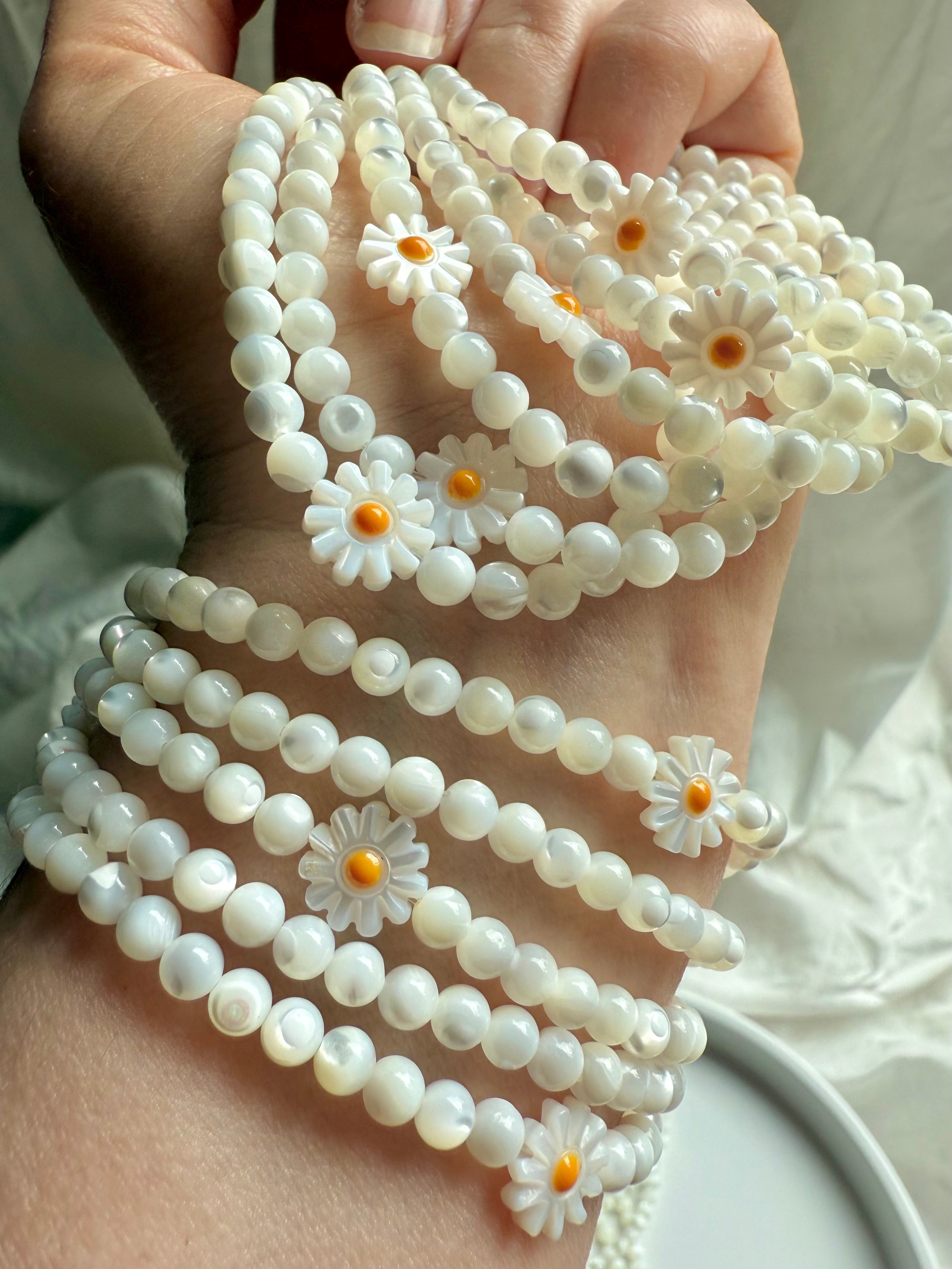 Close-up of Mother of Pearl daisy flower beads on opalescent white shell bracelet – floral gemstone jewelry for joy and lightness