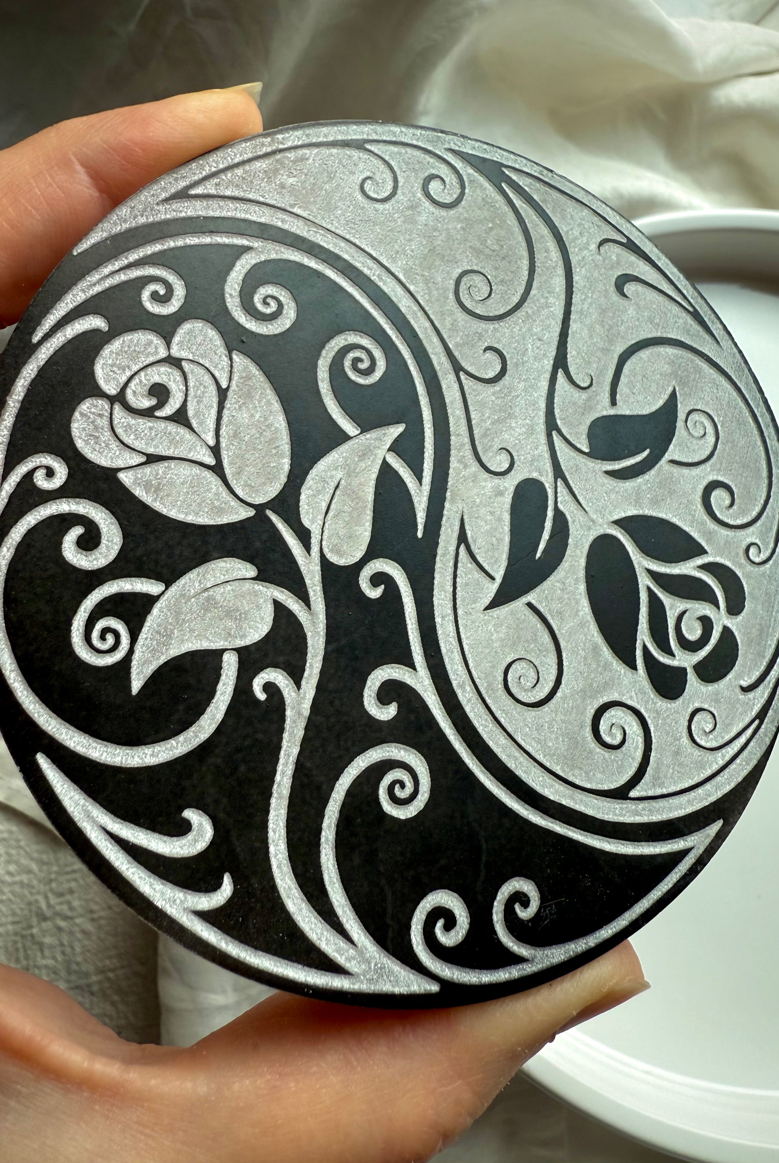 Hand holding yin yang rose selenite charging plate showing carved floral design for spiritual energy clearing