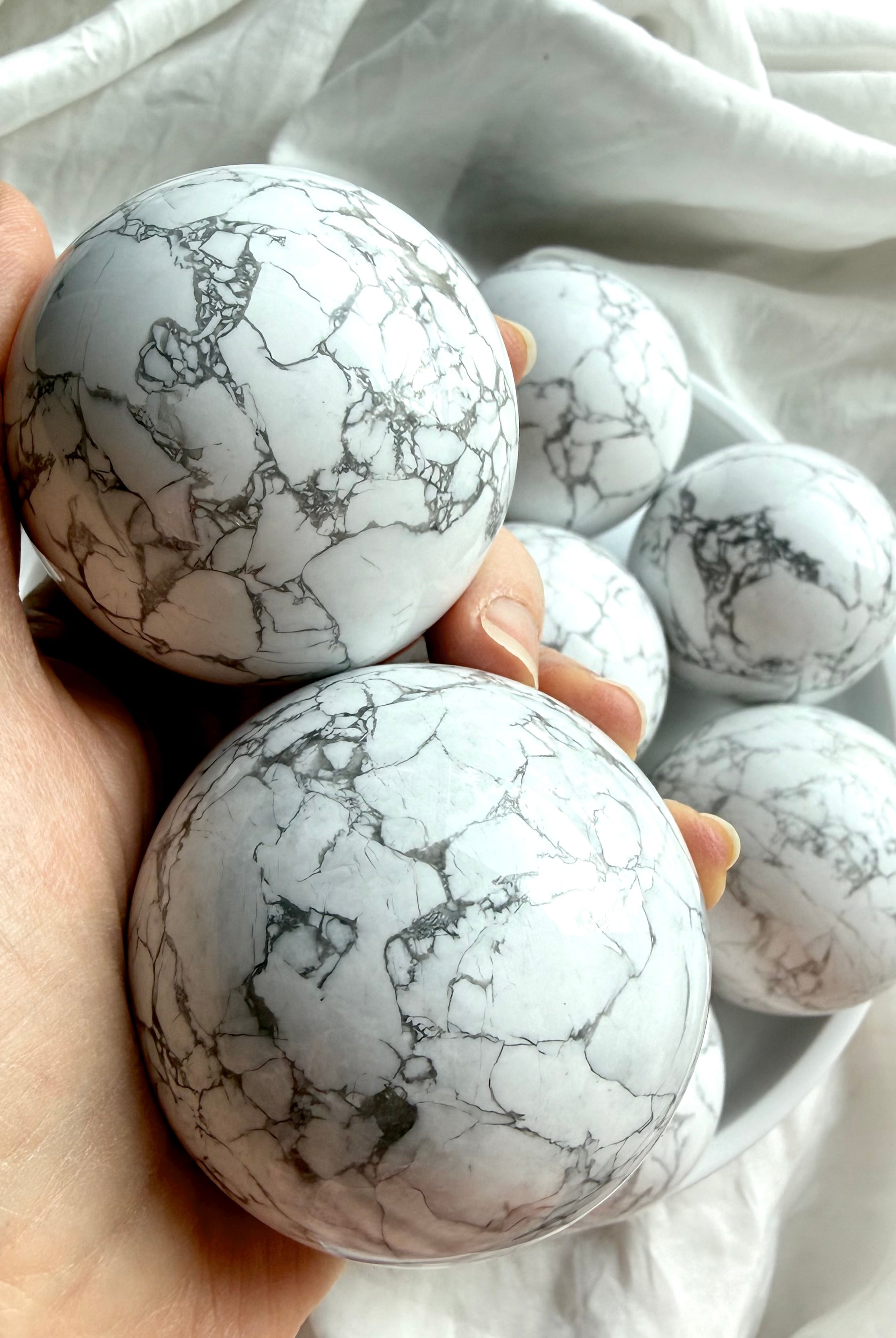 Closeup of two Howlite spheres in hand for size reference, polished white stone with gray marbling for calm and stress relief