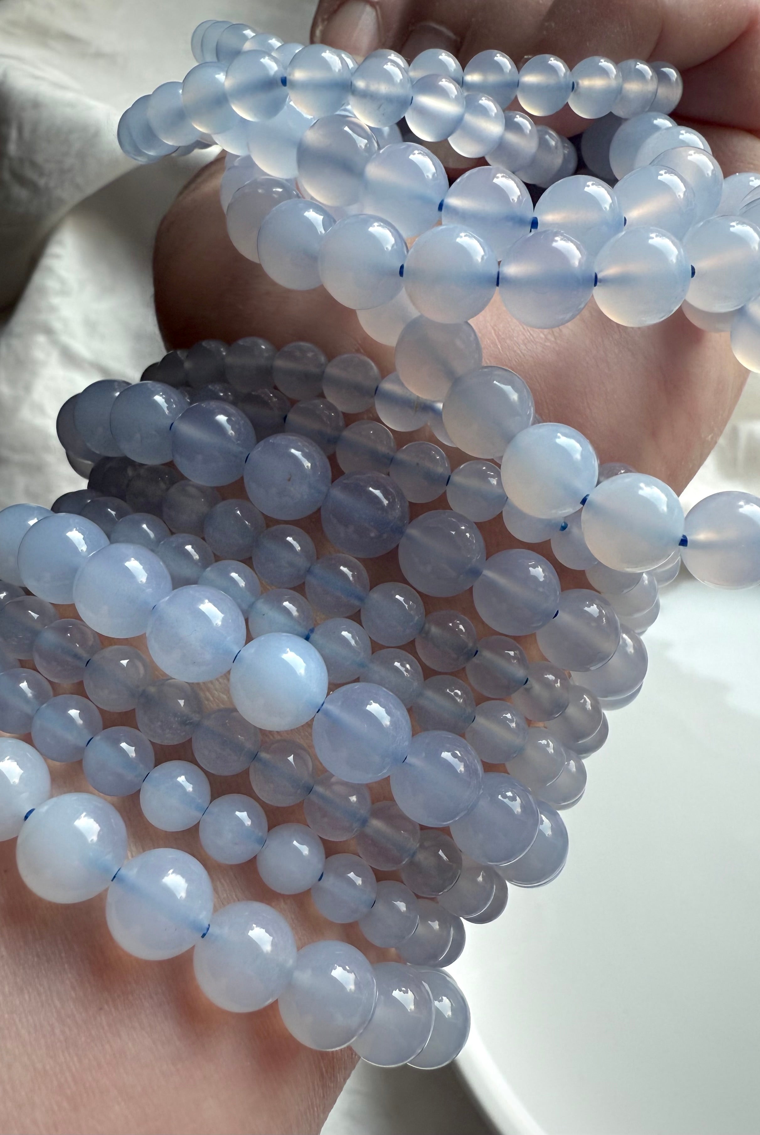 Multiple Blue Chalcedony crystal bead bracelets layered on arm — polished translucent blue gemstones for peace and emotional healing.