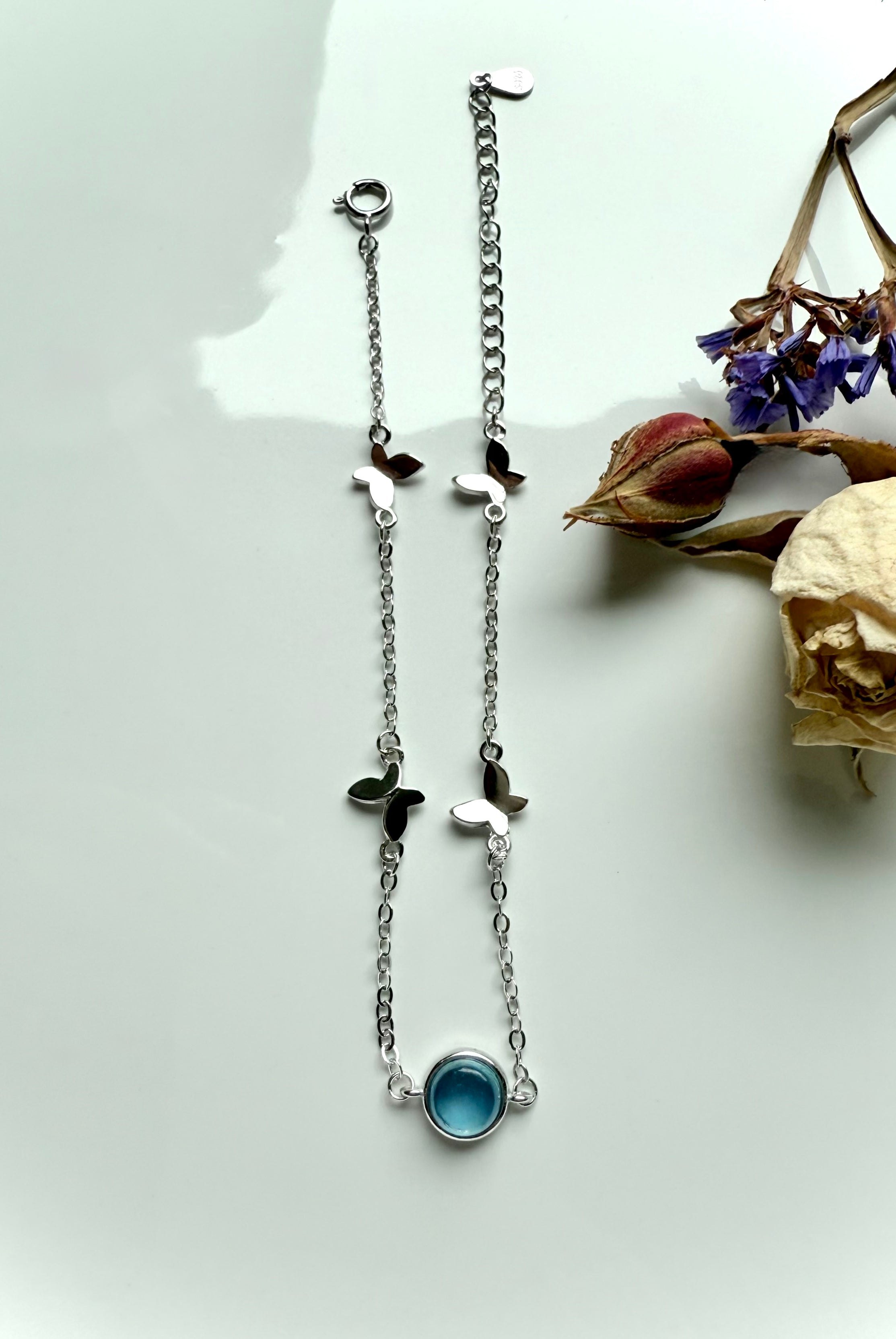 Aquamarine silver bracelet with butterfly charms styled beside dried rose and statice flowers, crystal jewelry for peace and calm