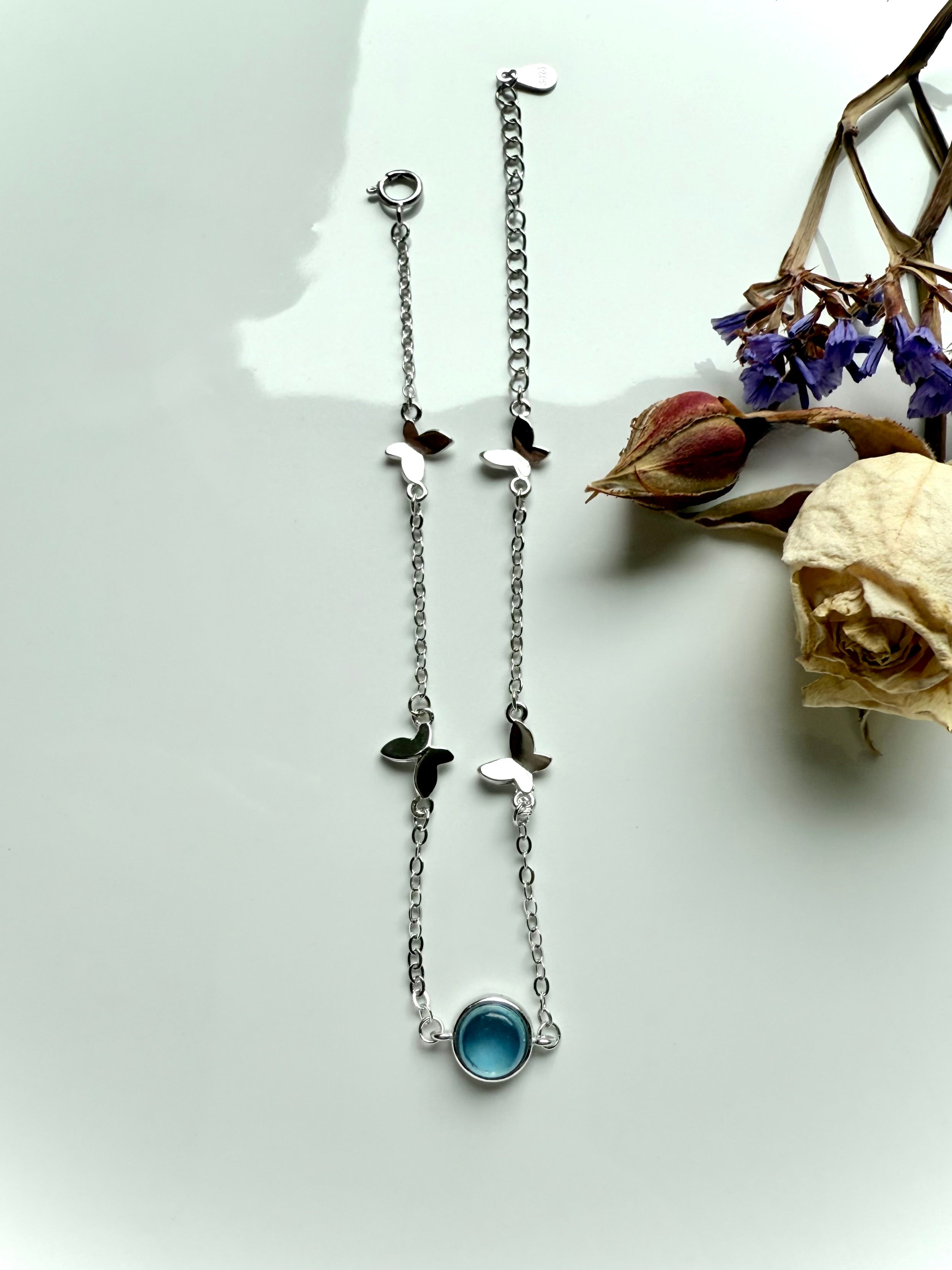 Aquamarine silver bracelet with butterfly charms styled beside dried rose and statice flowers, crystal jewelry for peace and calm