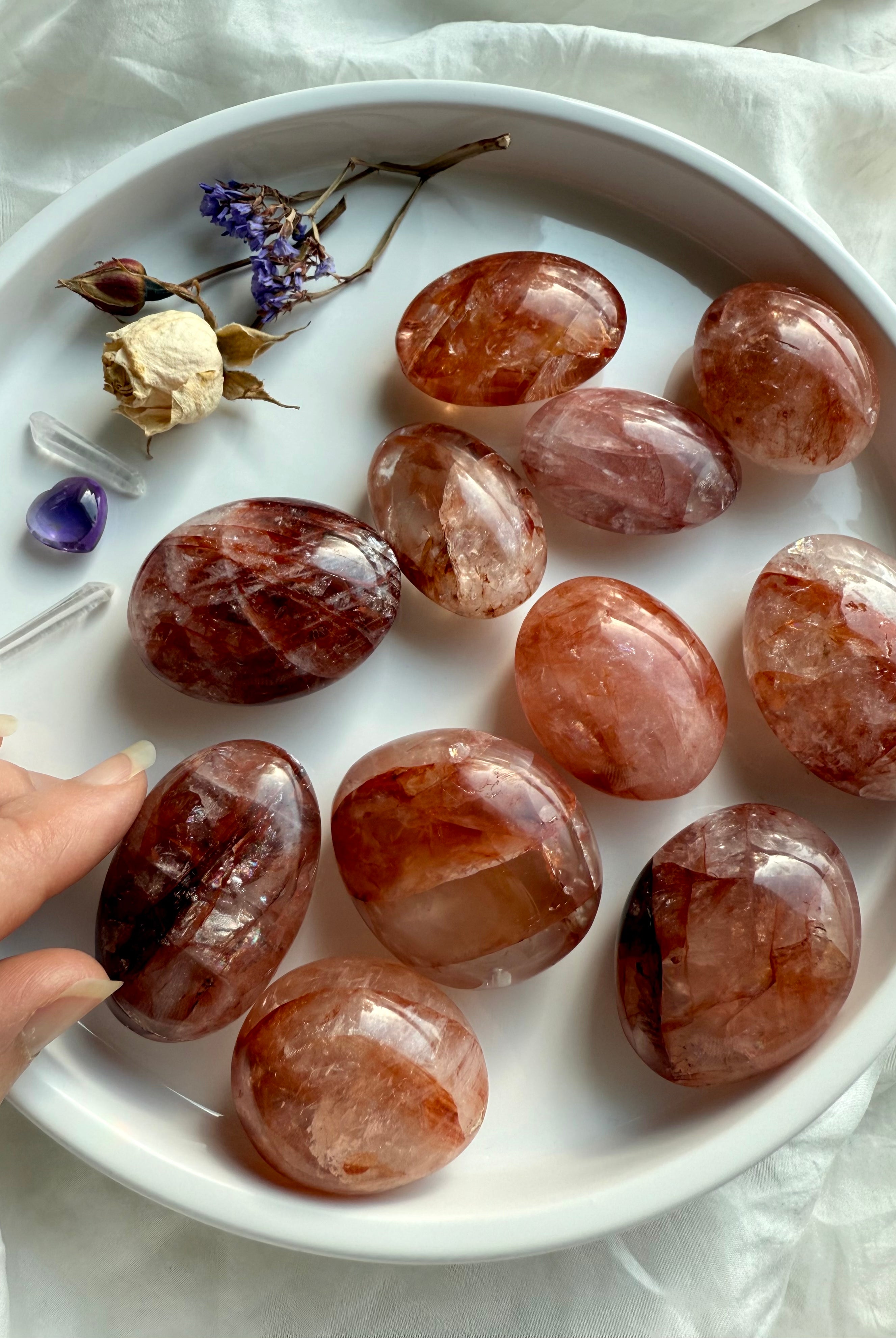 Fire Quartz palm stones with red and golden hematite inclusions displayed in a white dish for Root and Solar Plexus Chakra healing