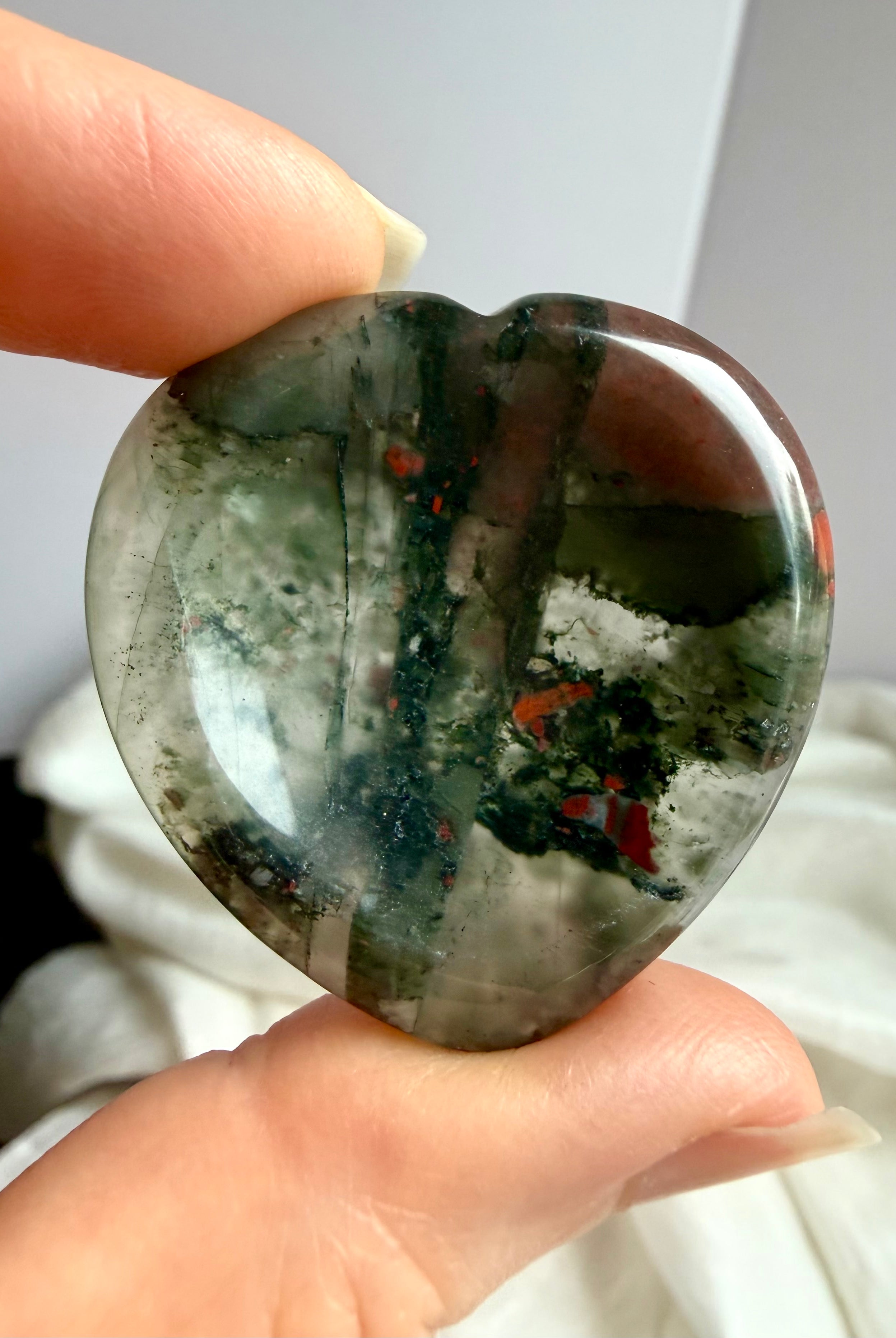 closeup hand holding bloodstone heart worry stone showing natural red flecks and polished finish, crystal for courage resilience and emotional balance