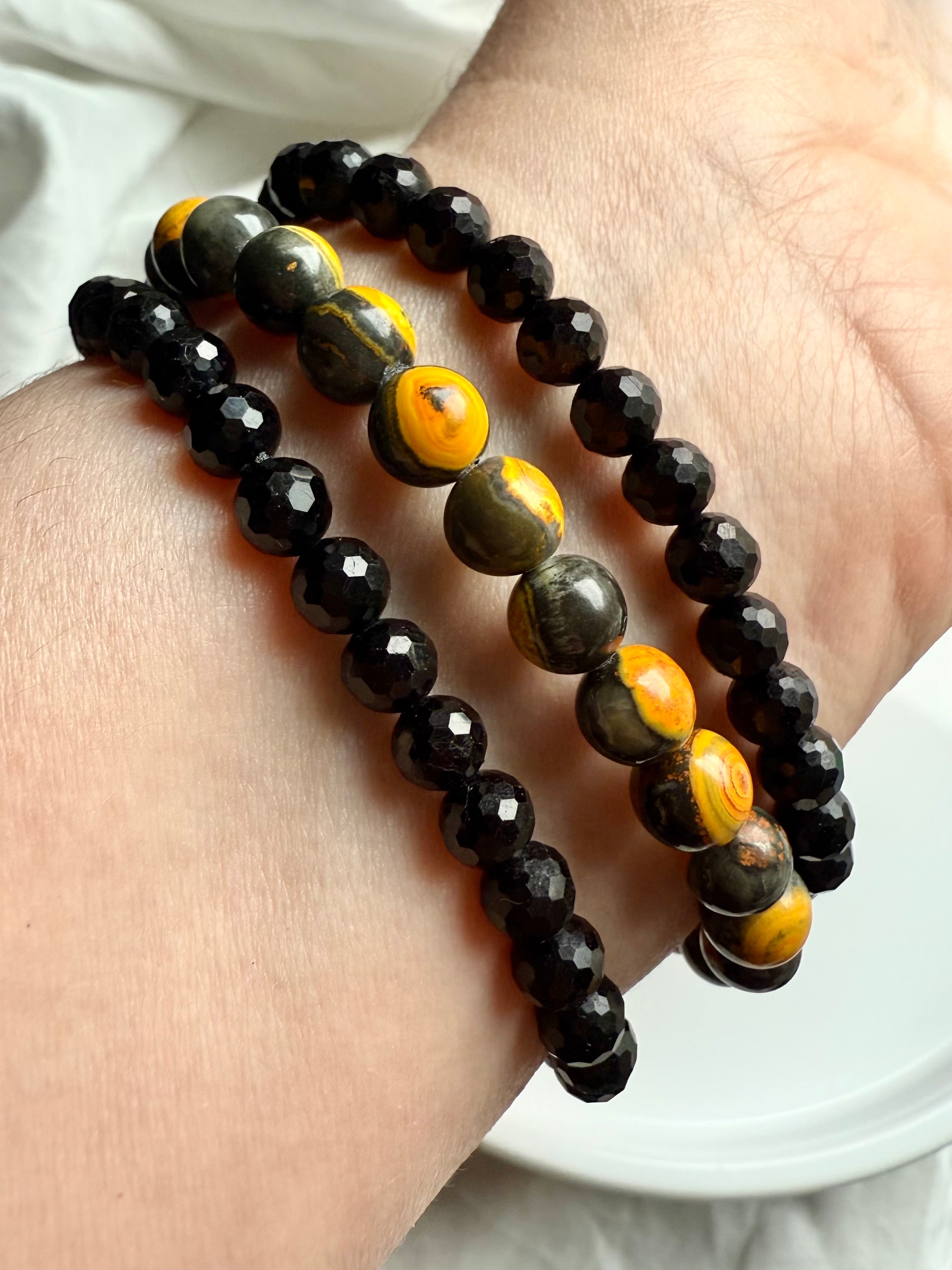 black tourmaline and bumblebee jasper bracelets stacked on wrist, combining bold protection with solar plexus activation
