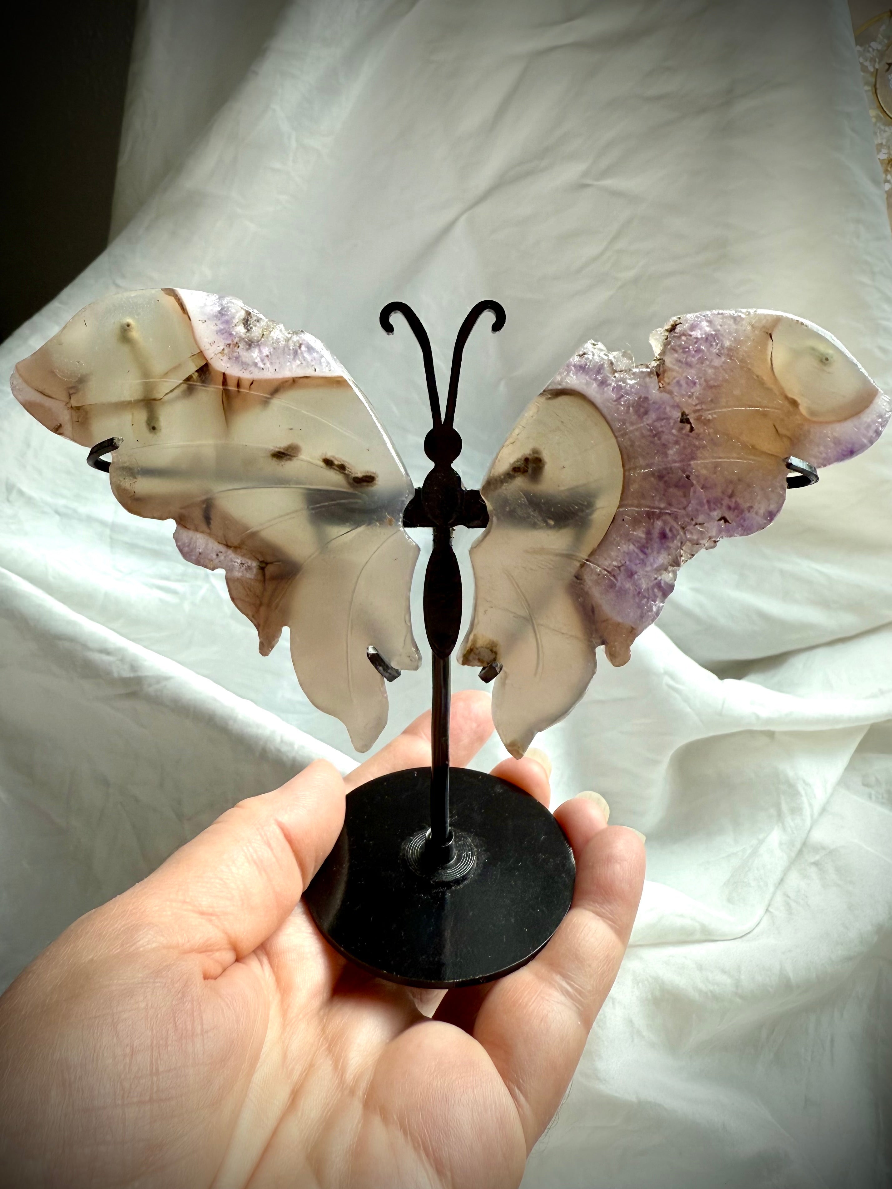 Druzy amethyst butterfly wings on metal stand held in hand, showing size and carved agate details.