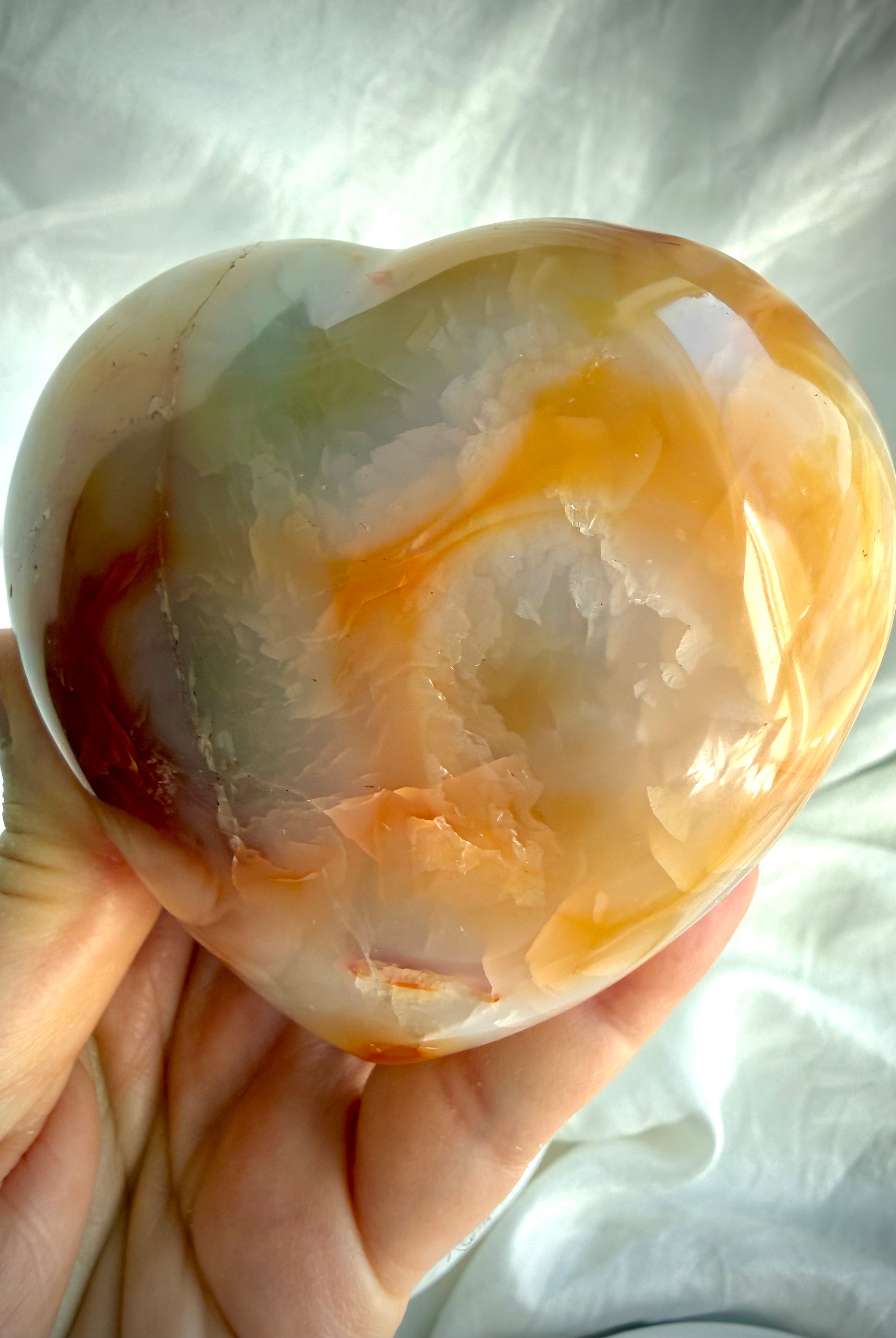 Large polished Carnelian heart with soft orange and cream swirls in natural light, one-of-a-kind healing crystal