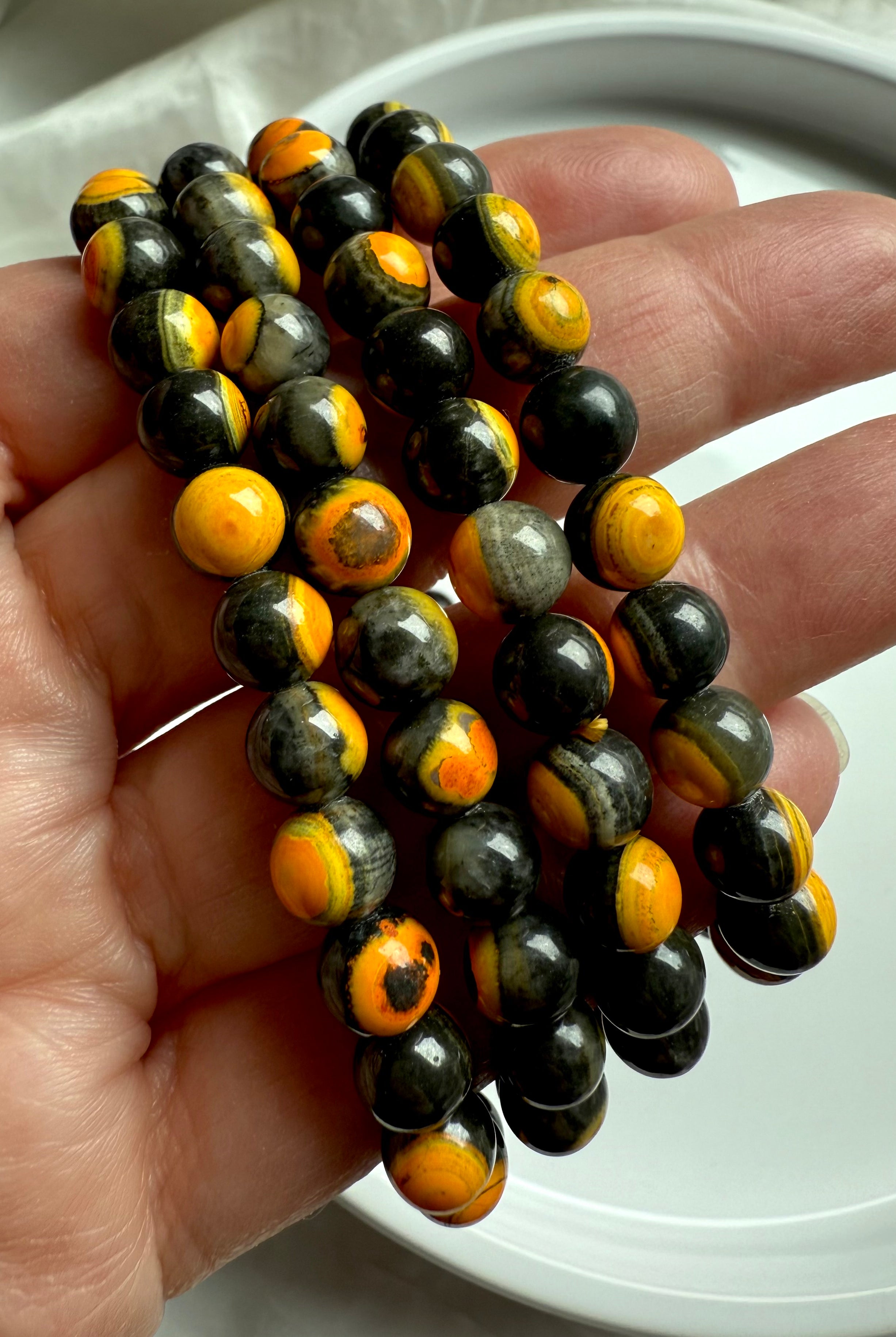Tight close-up of polished bumblebee jasper beads showing natural mineral layering in vibrant solar plexus tones of black, gold, and orange