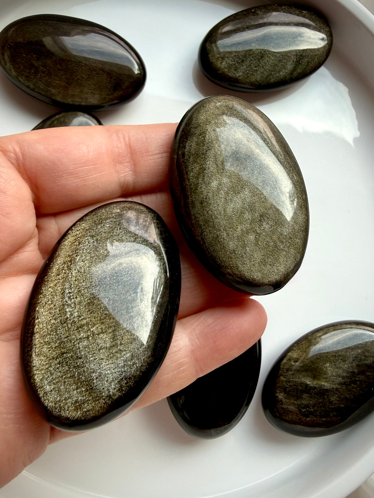 Golden Sheen Obsidian palm stones held in hand showing natural variations in golden shimmer and polished oval shapes