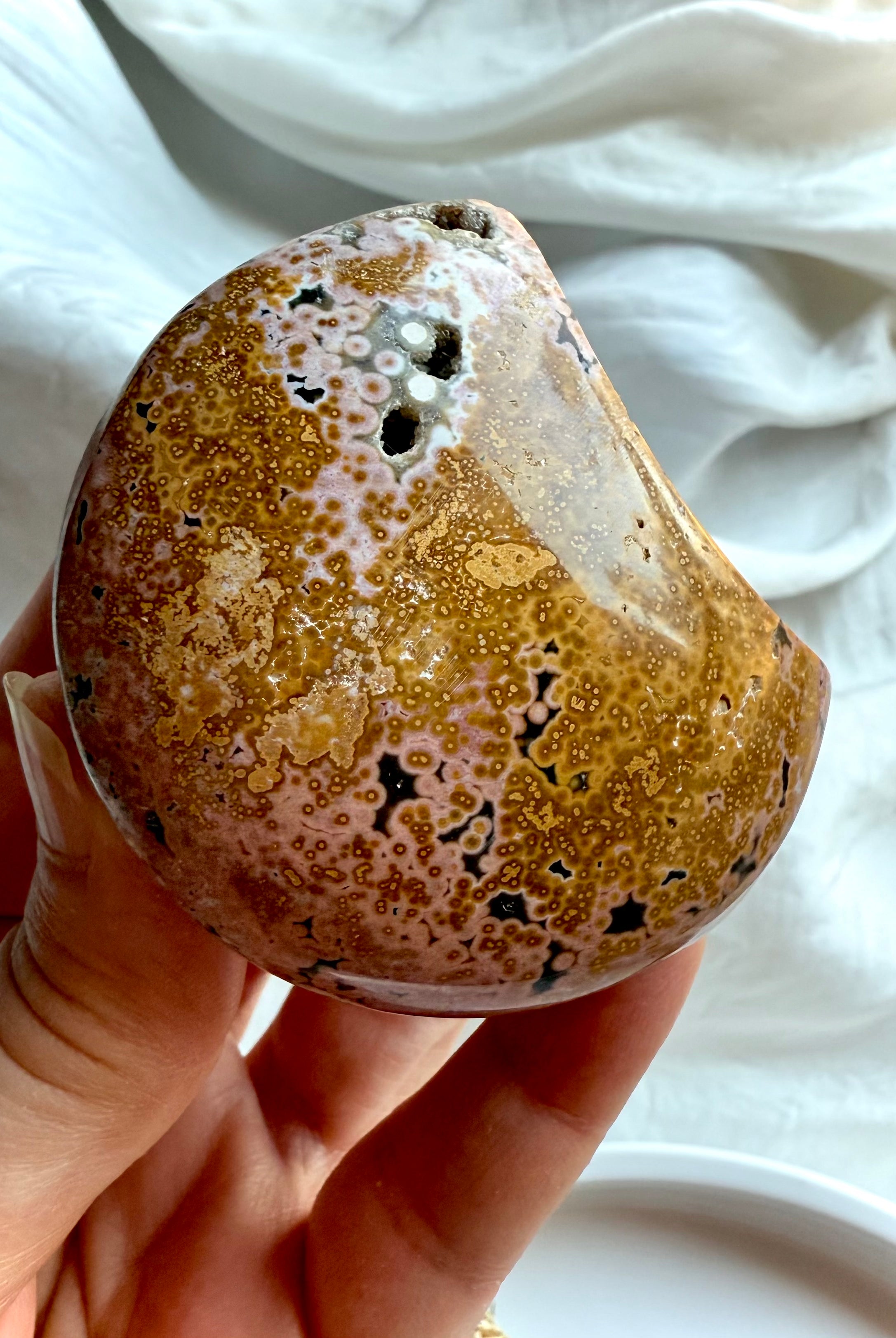 ocean jasper moon carving with peachy pink and yellow orbicular patterns held in hand, a soothing emotional healing crystal for comfort and balance