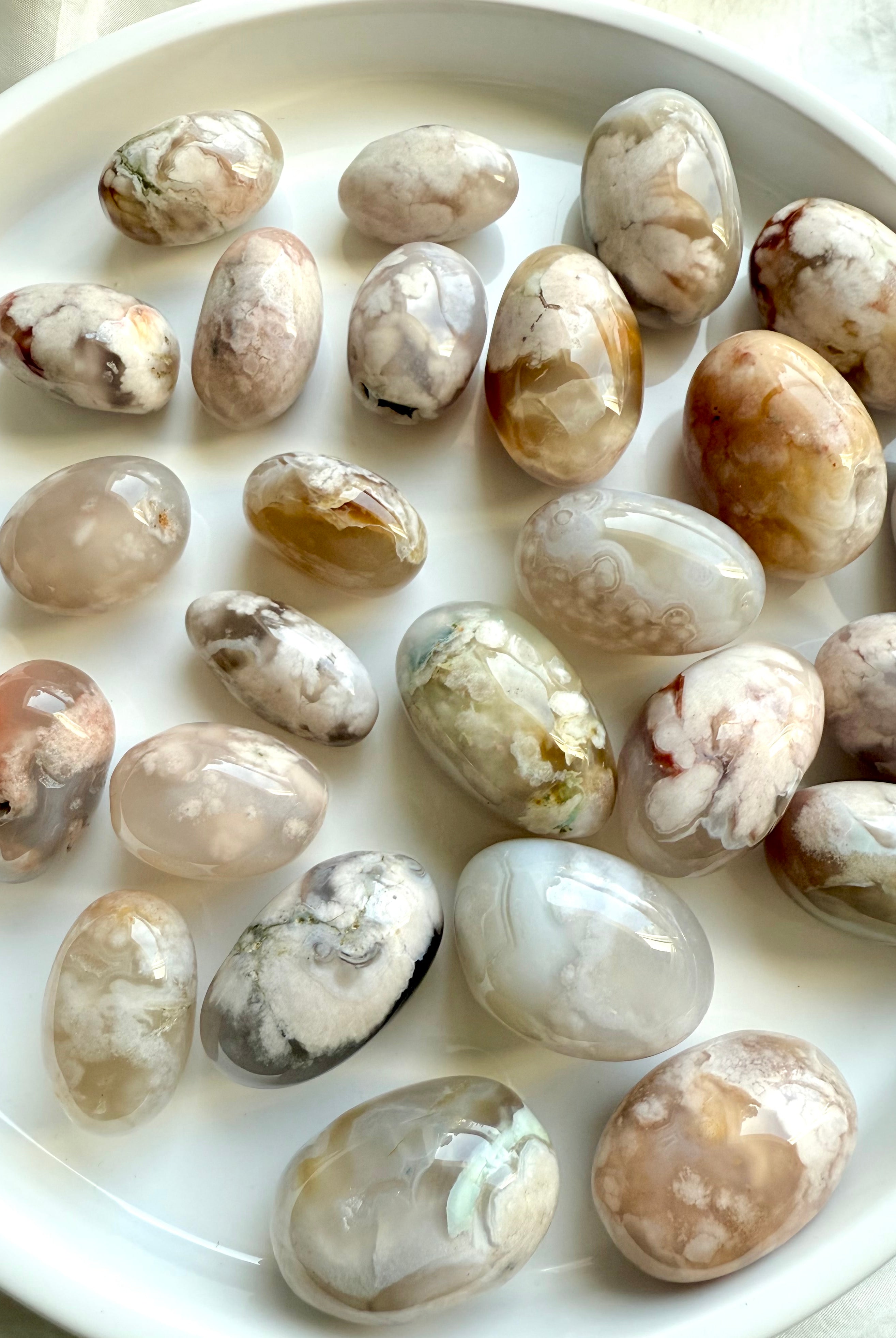 Two sizes of high quality Flower Agate tumbled stones with beautiful pastel colors on a white plate