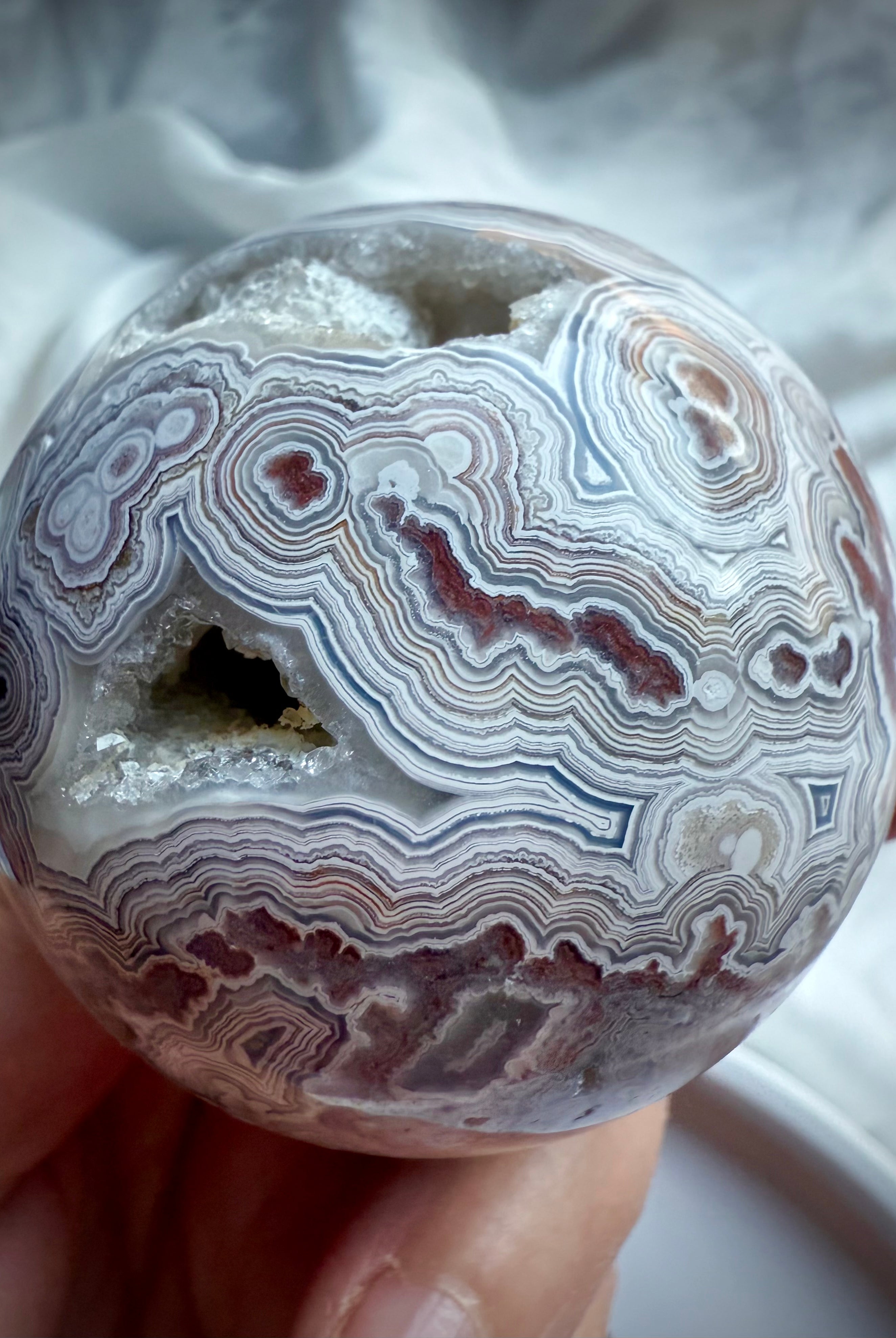 Detailed view of Crazy Lace Agate sphere with joyful swirling patterns, grounding red hues, and sparkling quartz inclusions