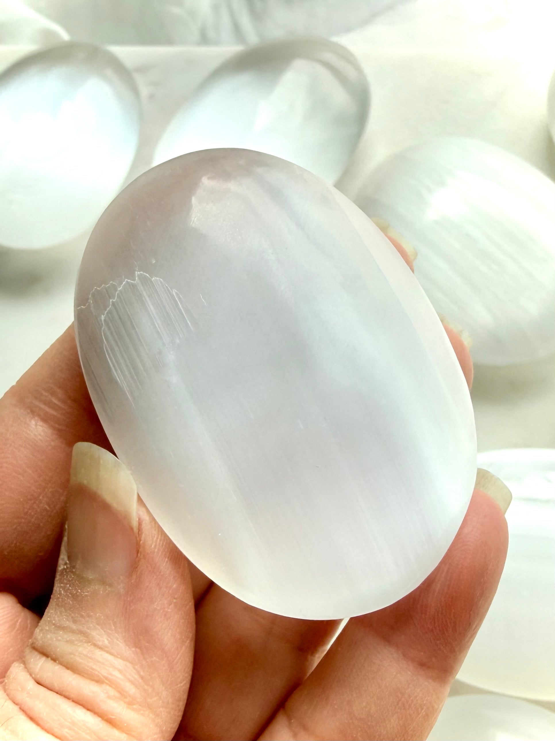 White Selenite palm stone with radiant pearlescent sheen, polished finish, and soft linear crystal texture