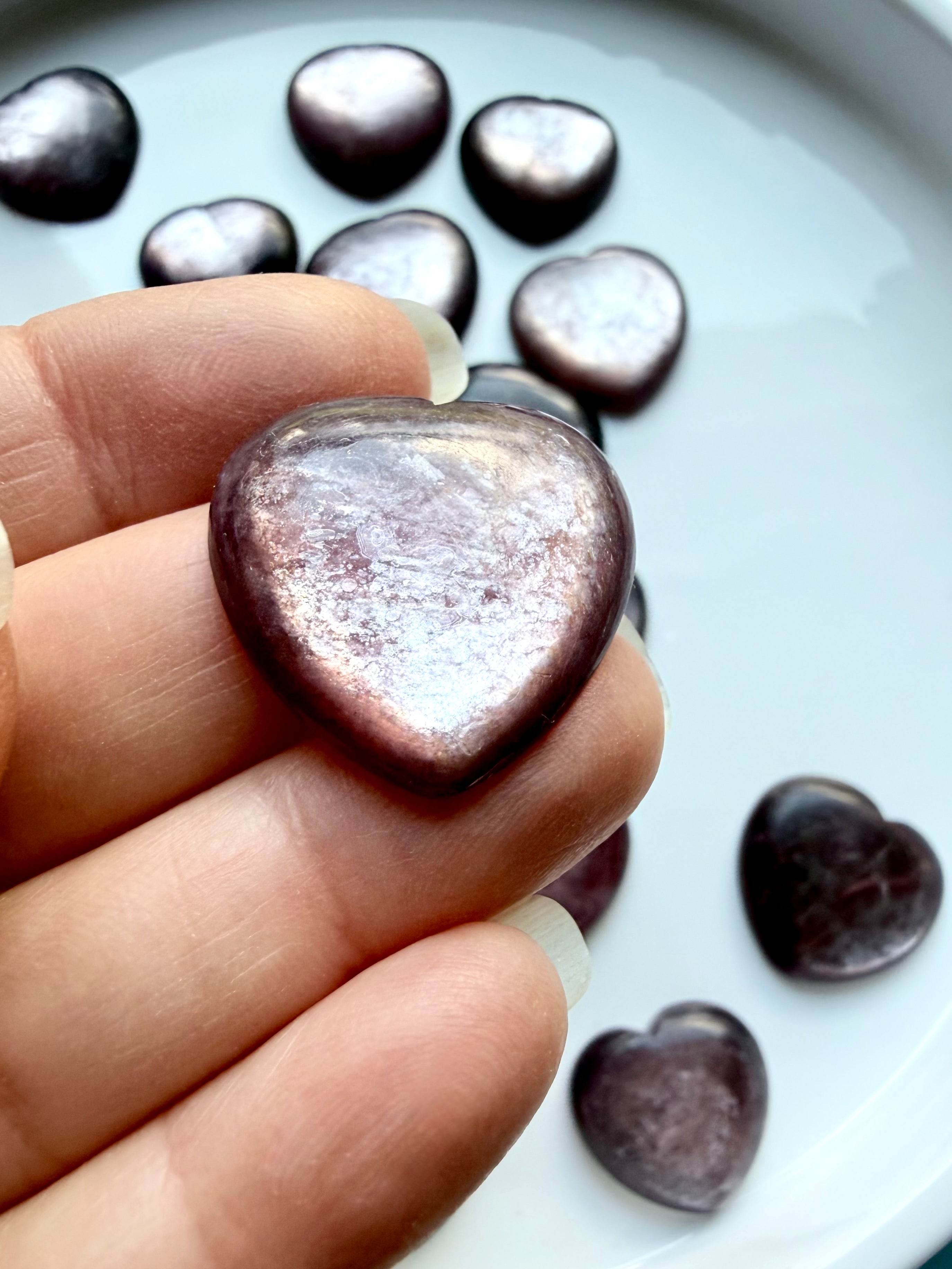 Hand holding gem lepidolite heart, purple crystal with mica shimmer and smooth polished surface