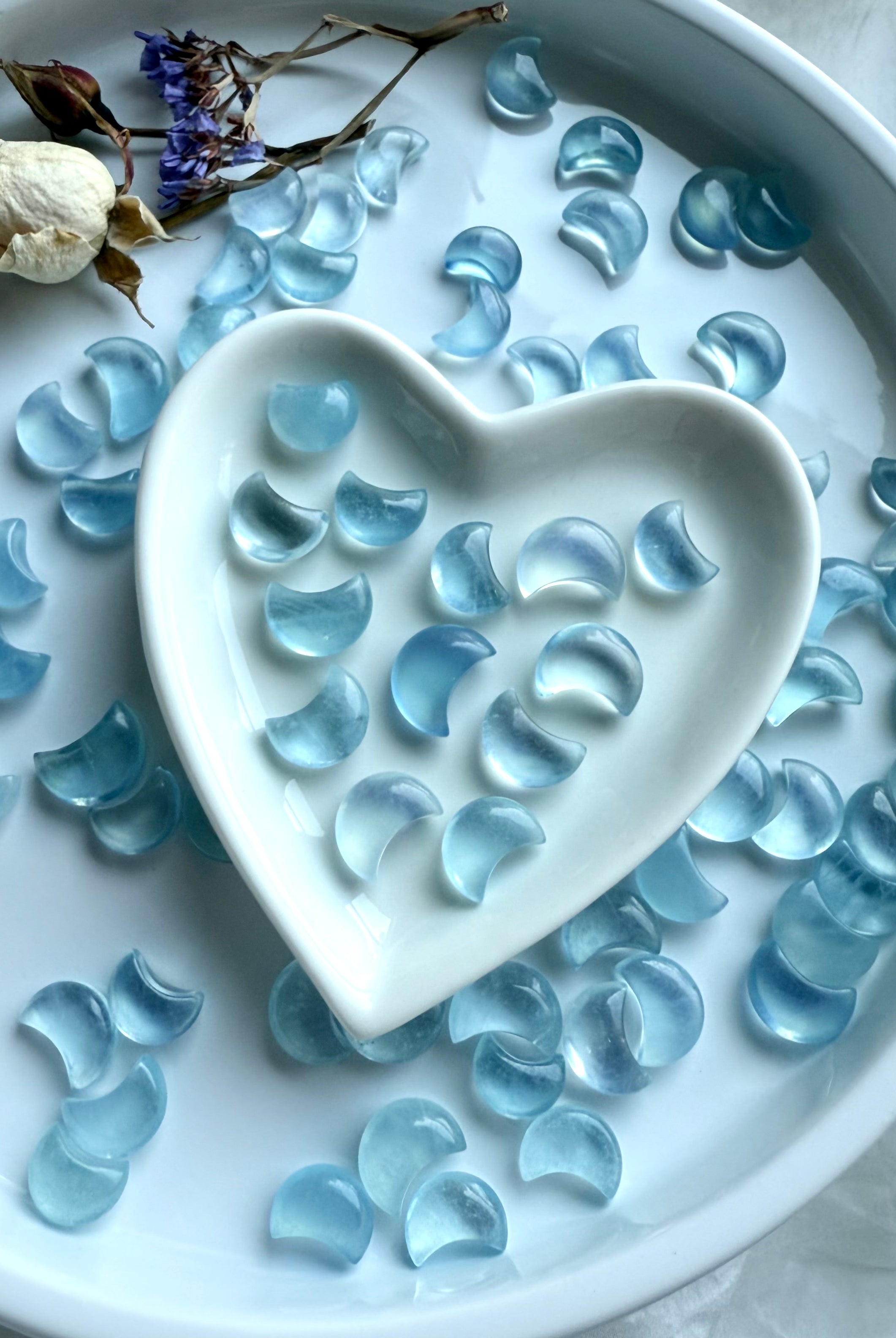 Moody crystal styling with Aquamarine moons scattered around and inside a heart dish — altar-ready gemstones for throat chakra balance and calm