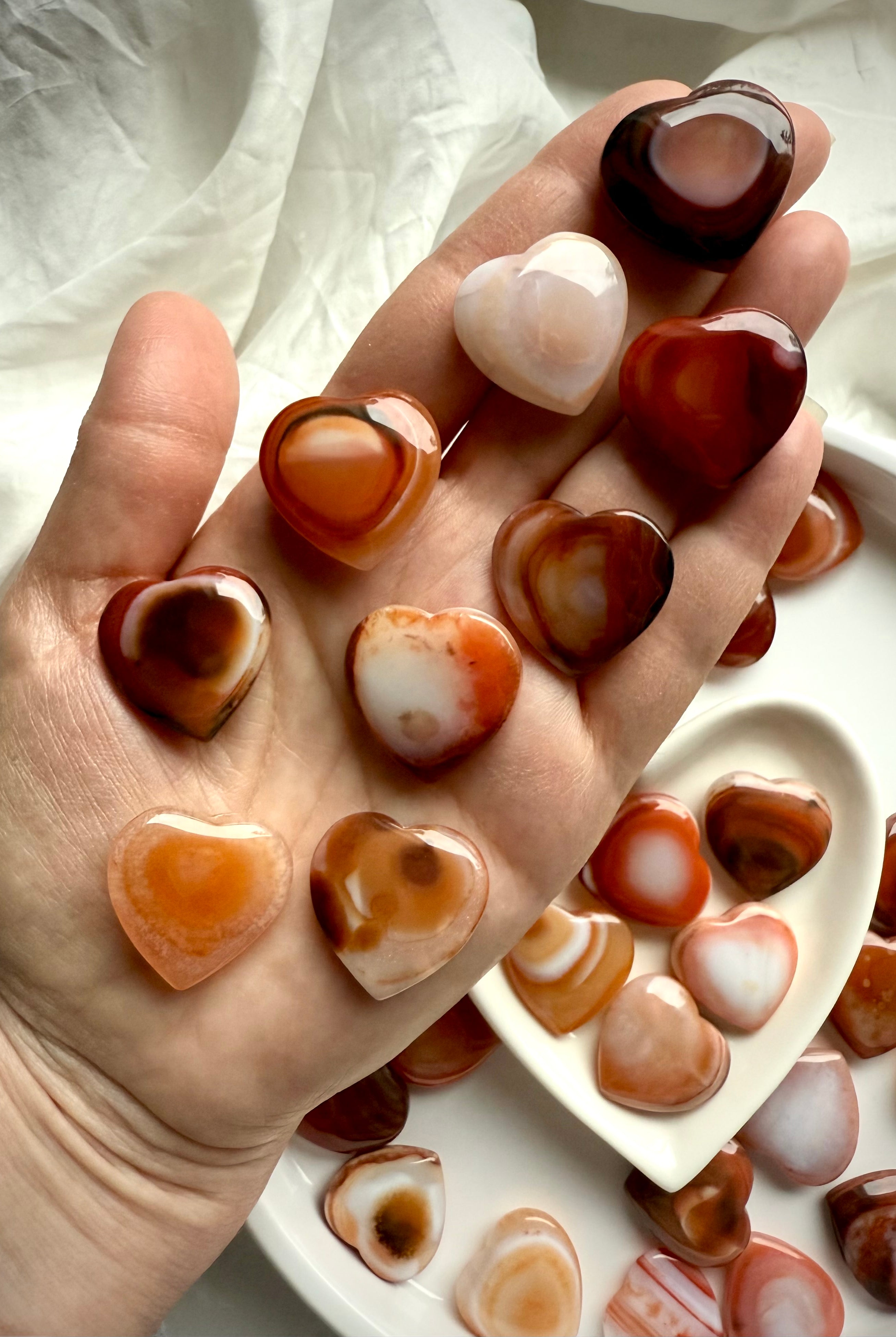 Collection of mini Carnelian heart crystals in hand, each with unique banded patterns, joyful sacral chakra healing stones