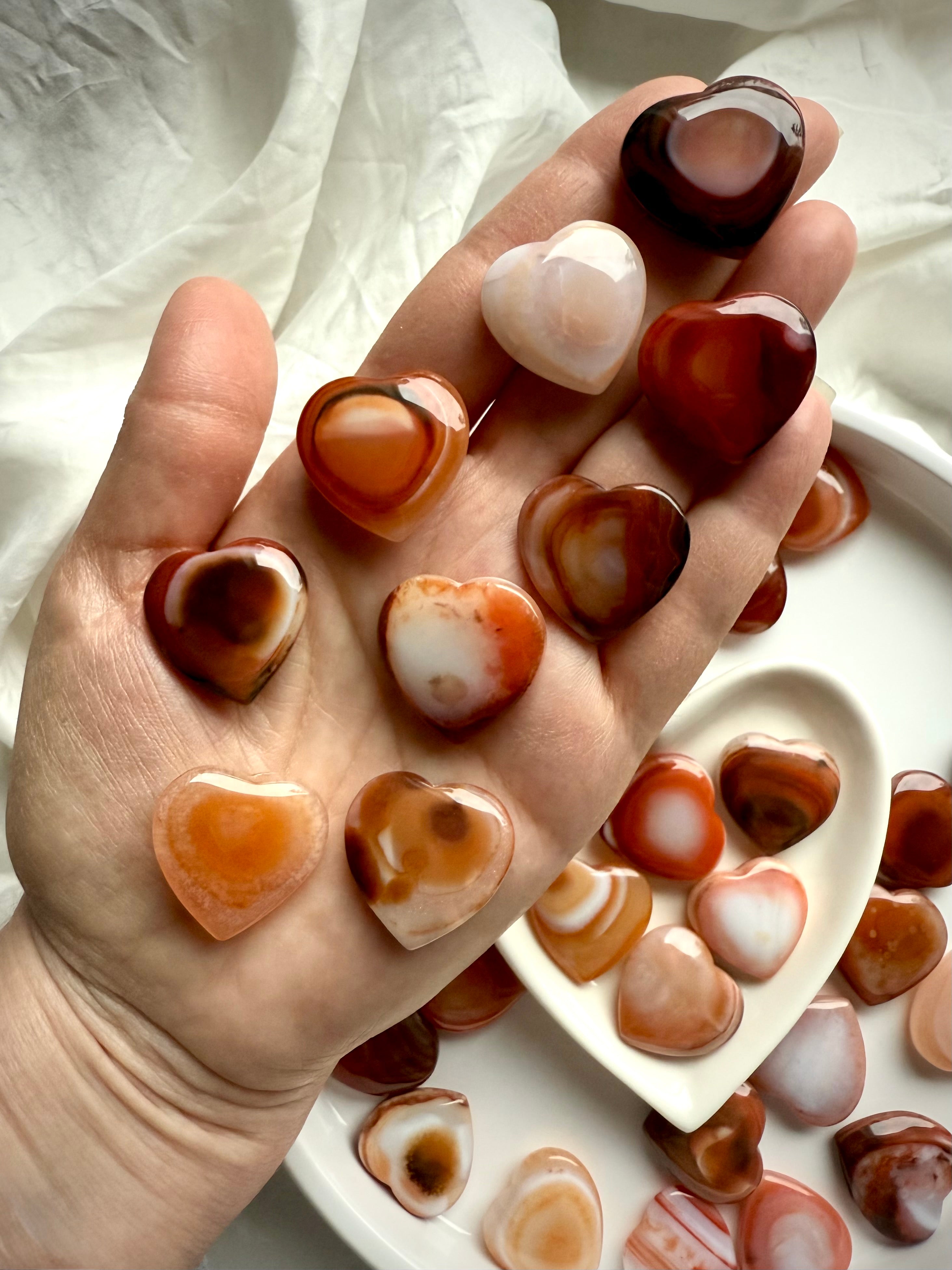 Collection of mini Carnelian heart crystals in hand, each with unique banded patterns, joyful sacral chakra healing stones