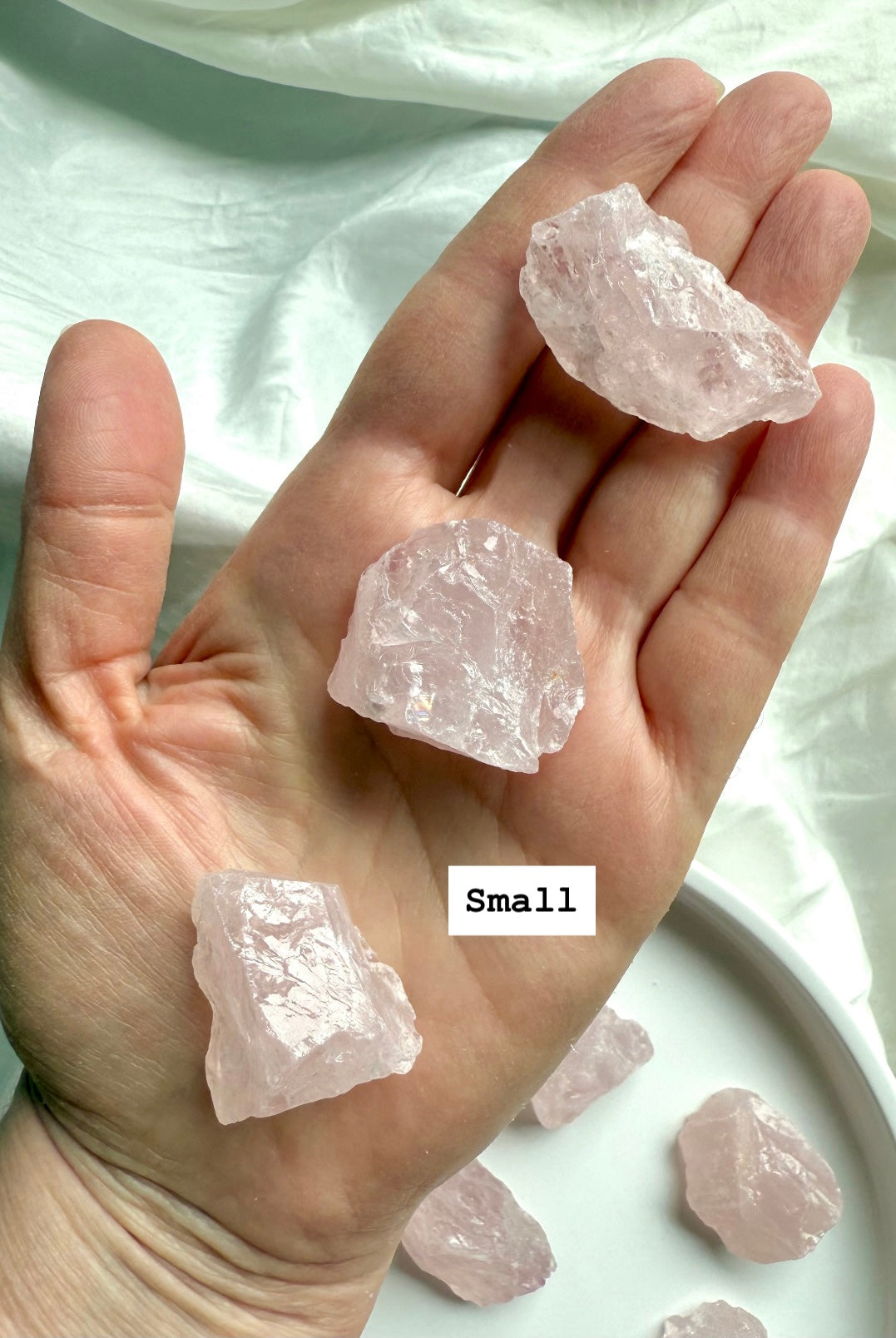 Hand holding three small raw Rose Quartz crystal chunks, pink healing stones for unconditional love and gentle energy support