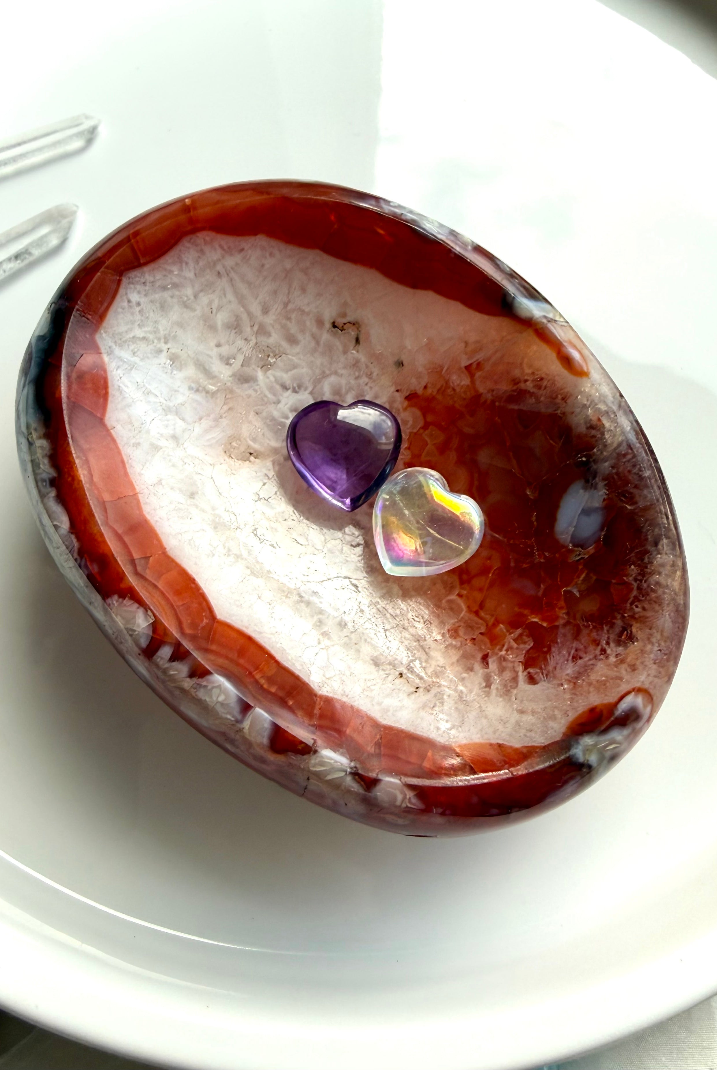 Carnelian agate bowl with druzy quartz center and translucent red edges holding 2 crystal hearts