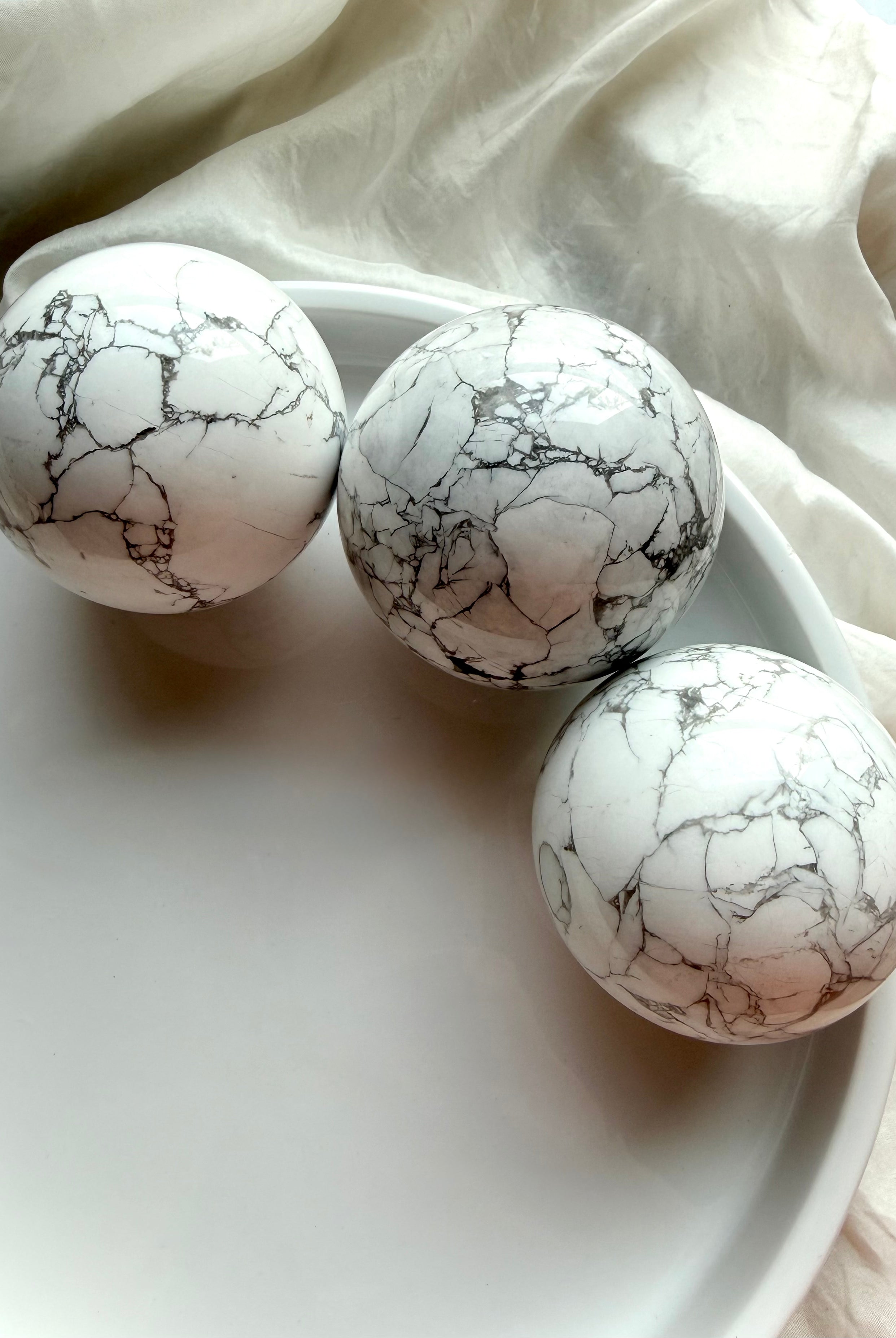 Three Howlite crystal spheres arranged in white tray, polished white stone with natural gray spiderweb veining for calm, sleep and anxiety relief