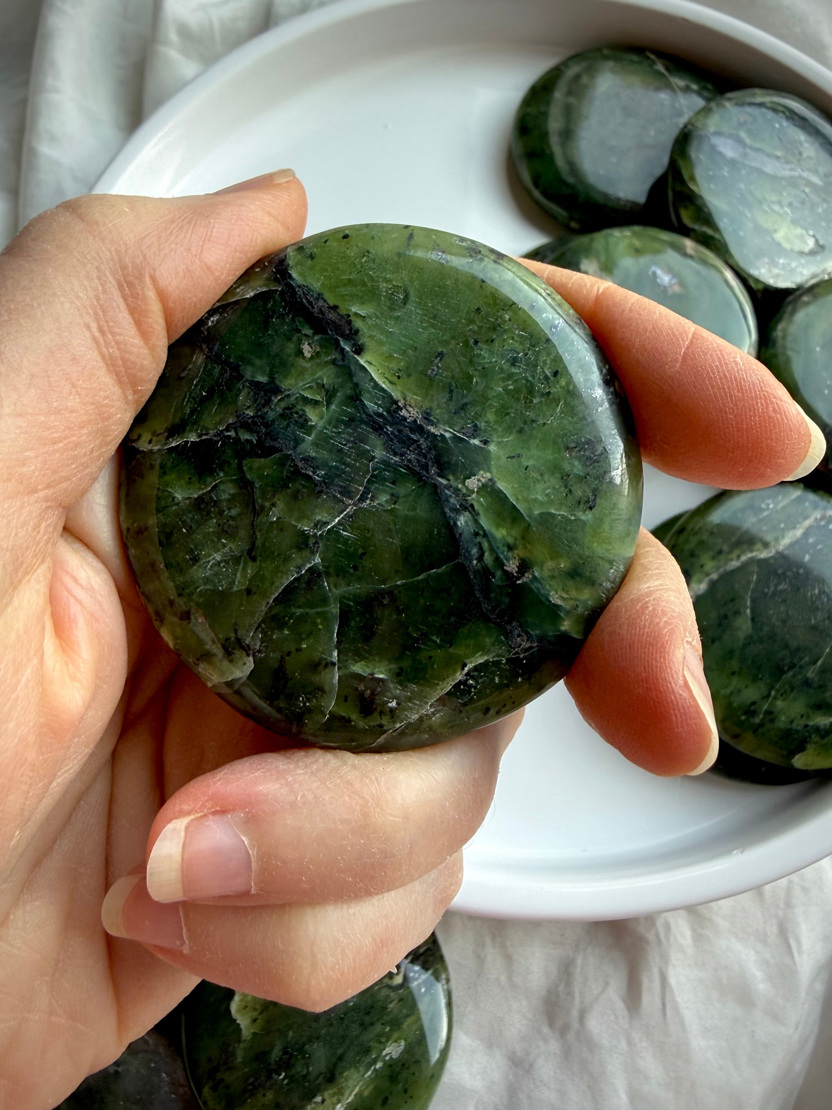 Nephrite jade palm stone in hand showing deep forest green tones and mineral veining, smooth heart chakra crystal for calming meditation