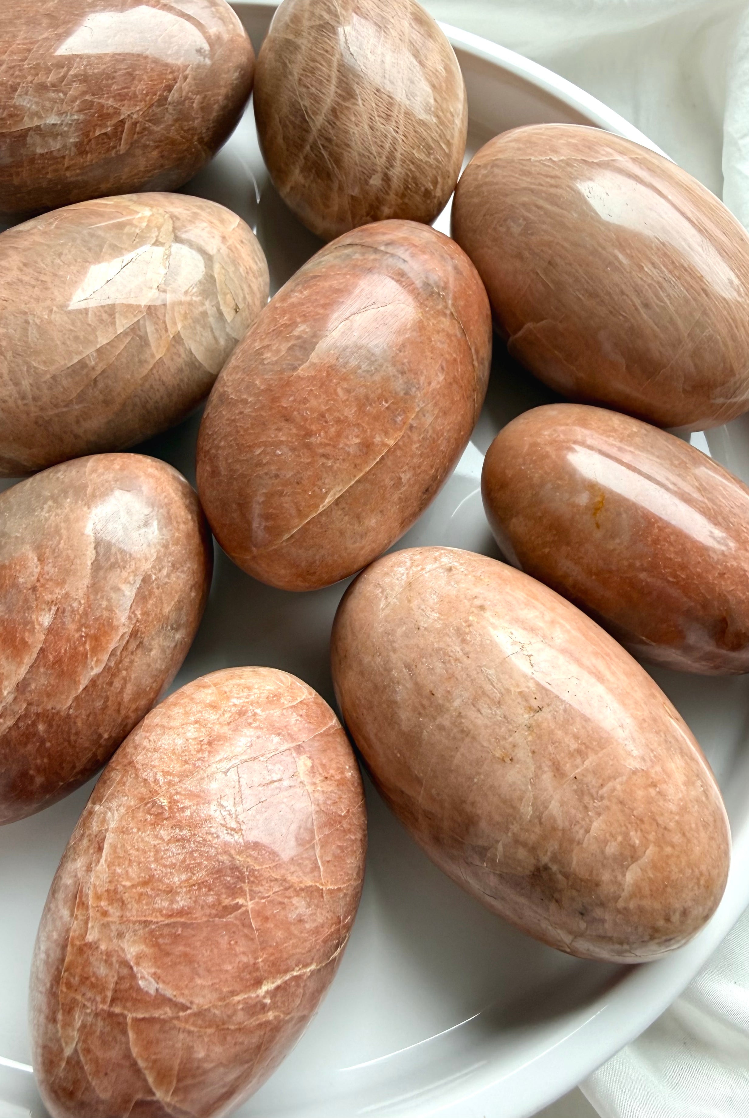 Large Peach Moonstone palm stones with warm peach and apricot tones on a white ceramic tray